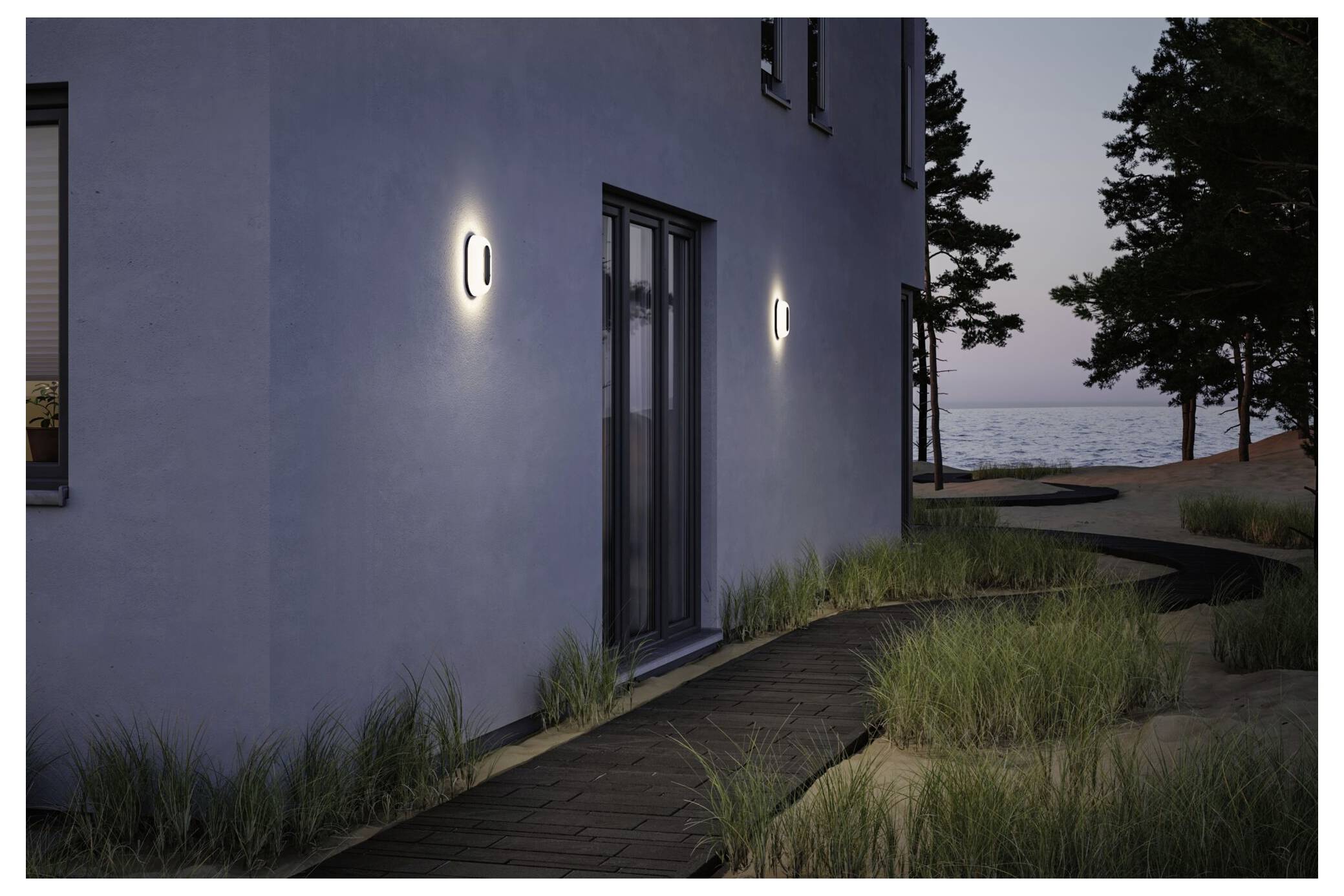 Modernes Hausäußeres bei Einbruch der Dämmerung mit leuchtenden Wandleuchten, einer Terrassentür, geschwungener Gehweg, Gräsern und einer entfernten Wasseraussicht unter Bäumen.