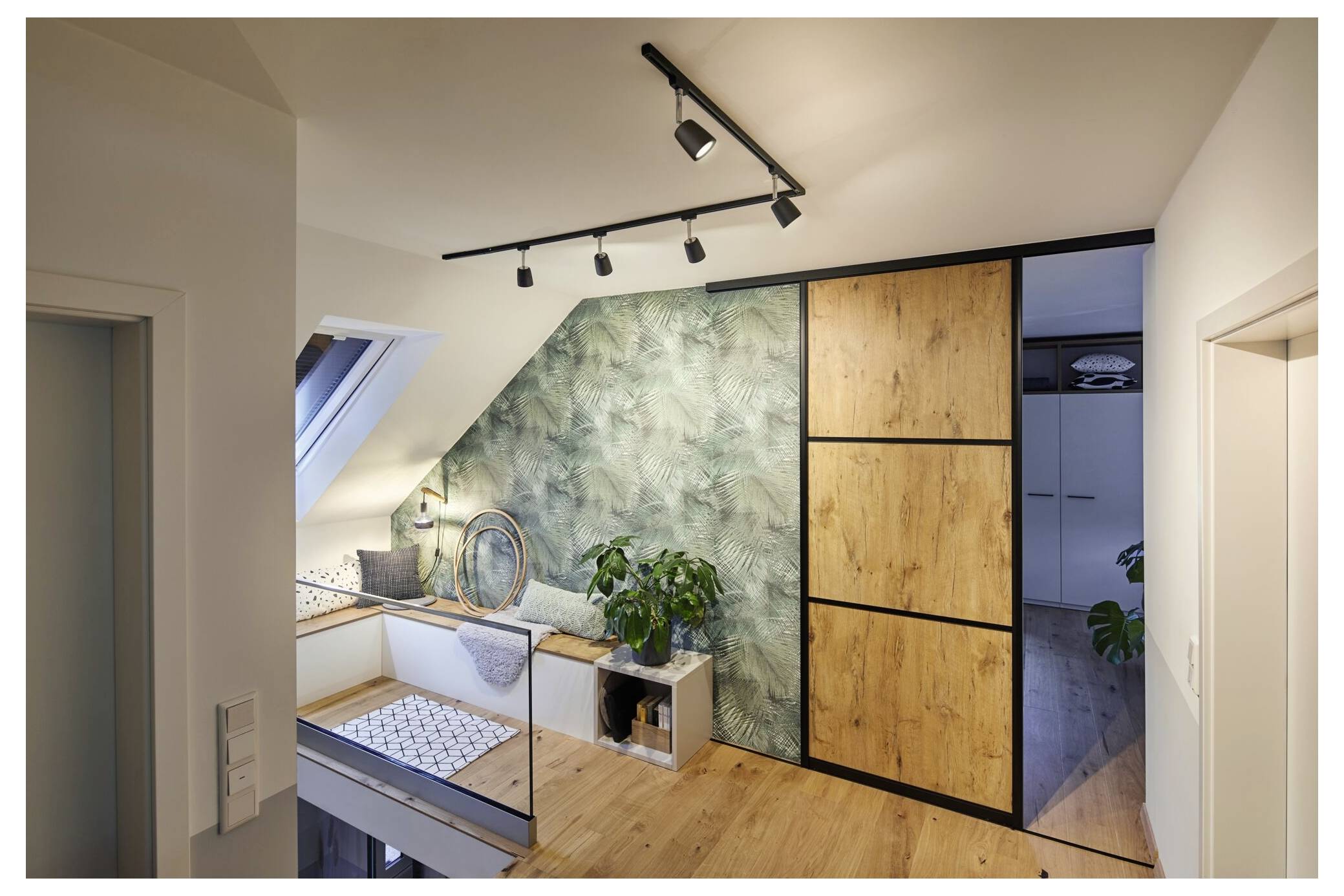 Modernes Dachzimmer mit schräger Decke, Holzboden, gemusterter Akzentwand, eingebauter Schreibtisch und Regalen sowie einer schwarzgerahmten Schiebetür zu einem Schrank oder angrenzenden Zimmer.