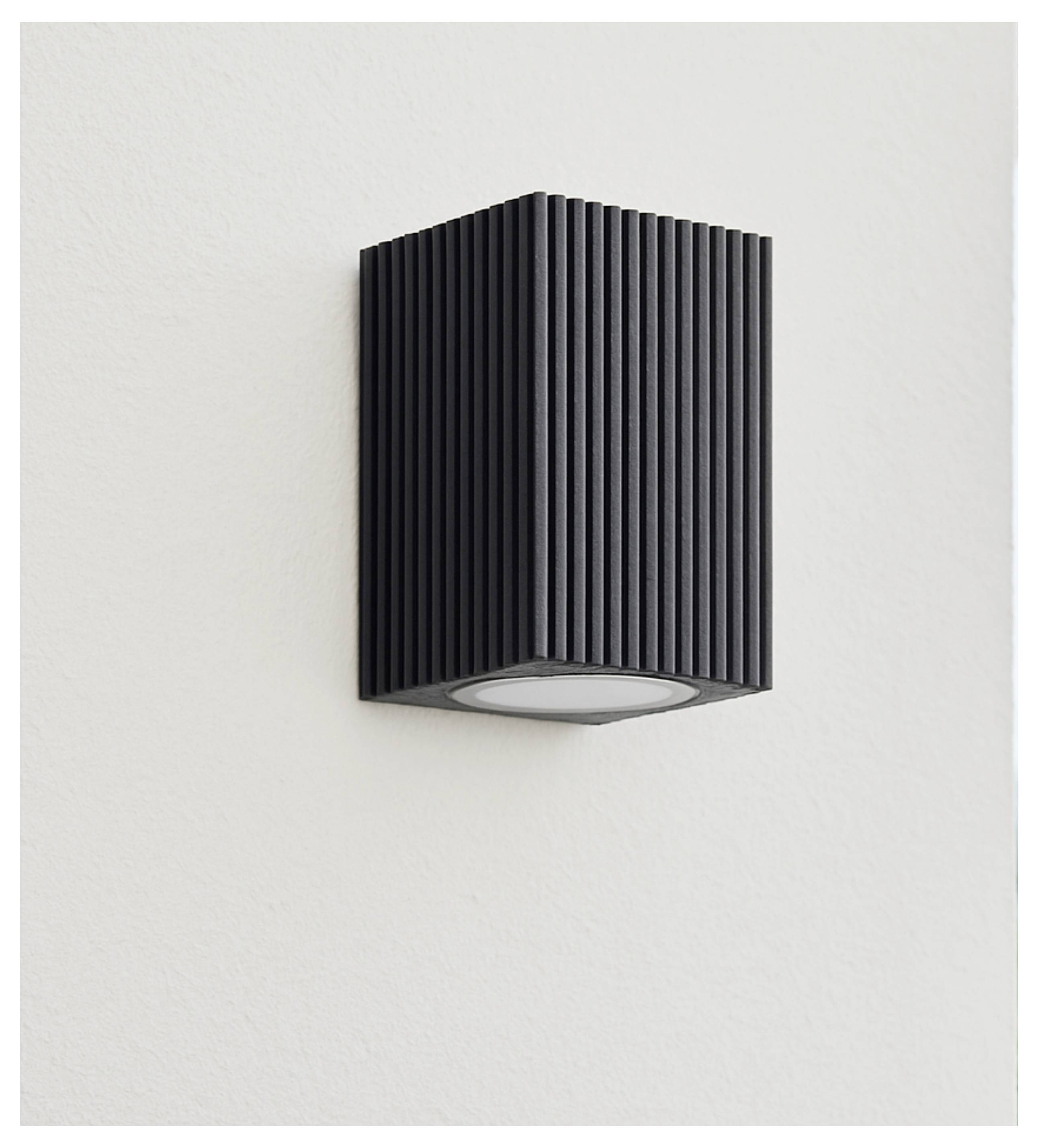 Schwarze gerippte rechteckige Wandleuchte auf einer hellen Wand montiert, mit einer ovalen nach unten gerichteten Lichtöffnung.