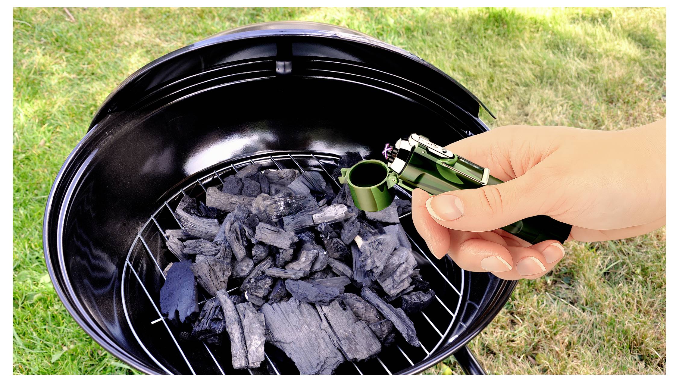 Hand hält ein grünes Feuerzeug über Holzkohle in einem runden Grill im Freien und bereitet sich darauf vor, das Feuer zu entzünden.