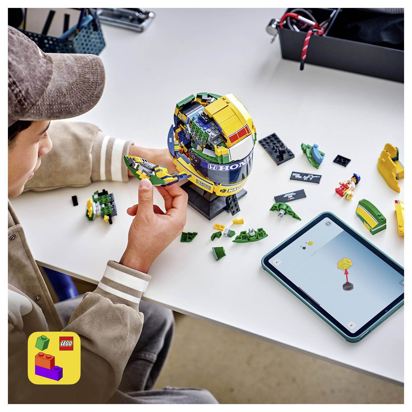 Ein Kind baut ein LEGO-Modell-Helm an einem Tisch, während es Anweisungen auf einem Tablet befolgt, mit verstreuten Steinen und Teilen in der Nähe.