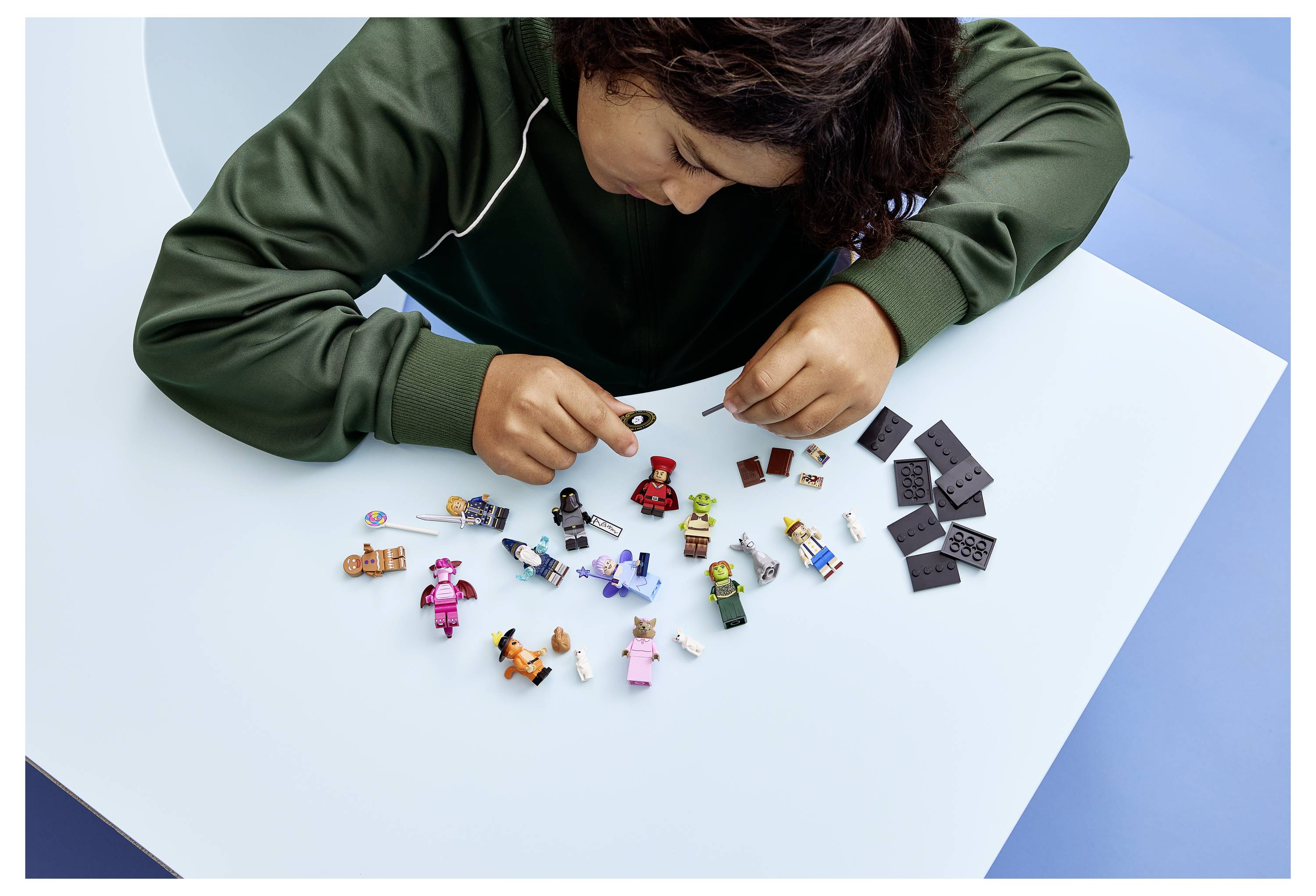 Kind, das kleine Spielfiguren und Teile auf einem Tisch zusammensetzt, bunte Minicharaktere und schwarze Teile für ein Bauprojekt organisiert.