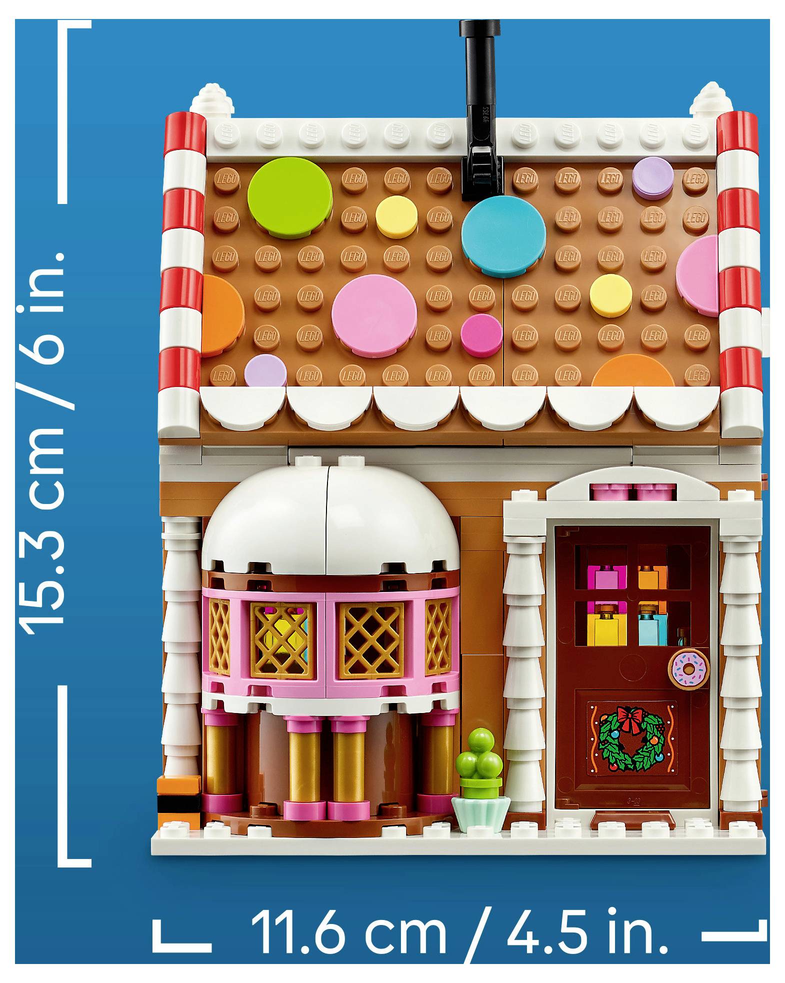 LEGO-ähnliches Miniatur-Süßigkeitenhaus mit buntem Streuseldach, rosa Fenstern, Haustür und Messbeschriftungen mit einer Höhe von 15,3 cm und einer Breite von 11,6 cm.