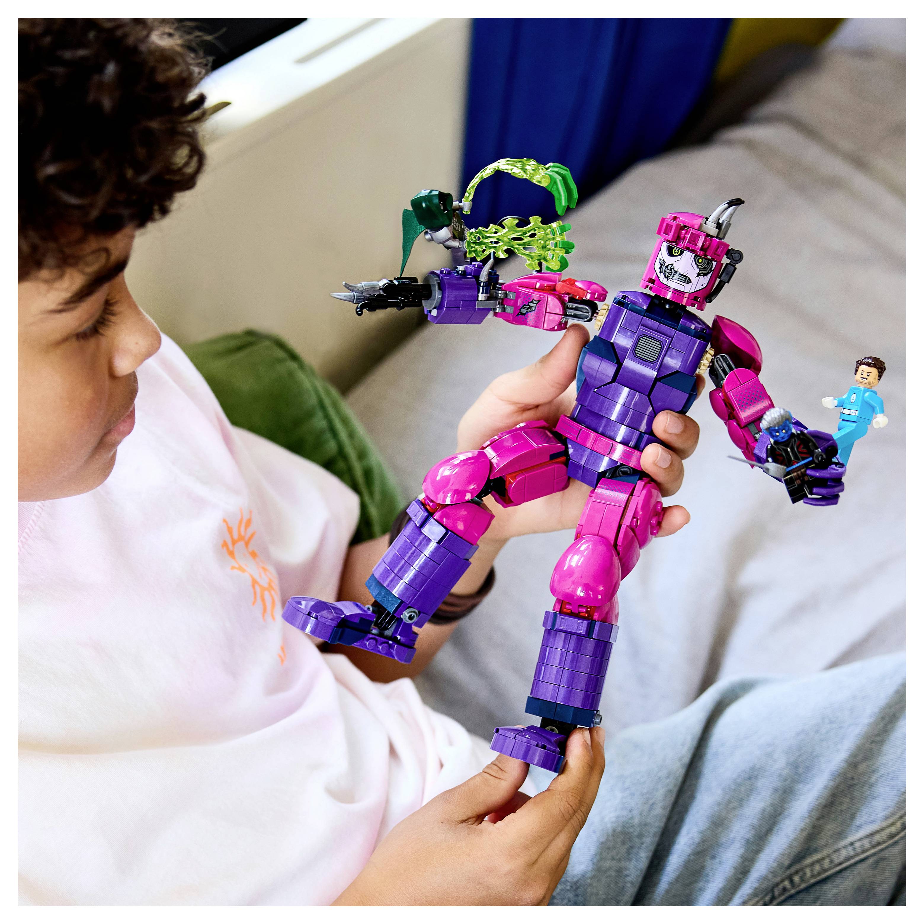 Kind, das ein buntes lila und rosa Roboterspielzeug mit einer kleinen Actionfigur hält, sitzt auf einem Bett oder einer Couch.