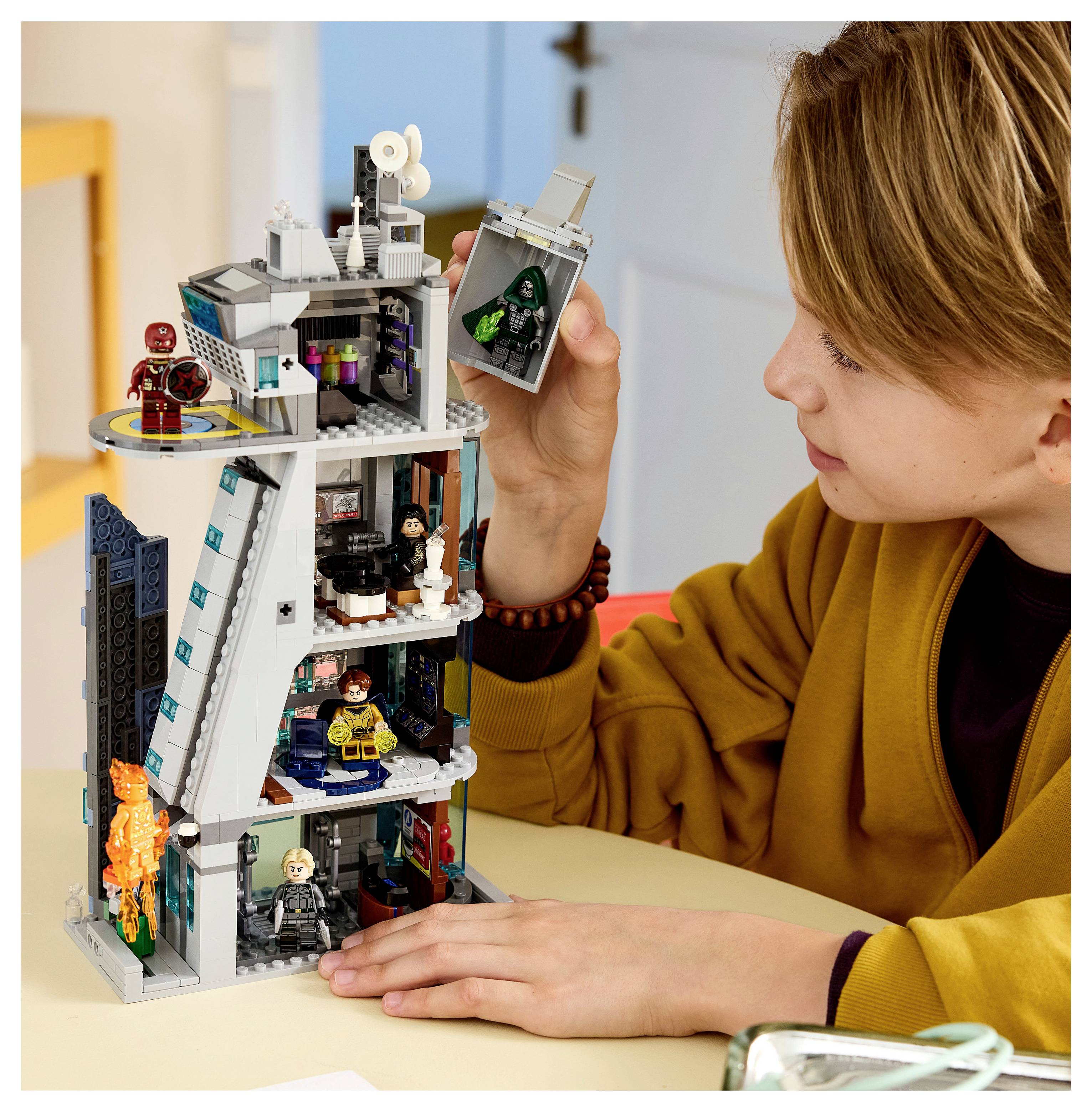 Ein Kind spielt mit einem LEGO-ähnlichen Wolkenkratzer-Set, hält ein Minifiguren-Teil in der Hand und schaut sich das gebaute Modell auf dem Tisch an.