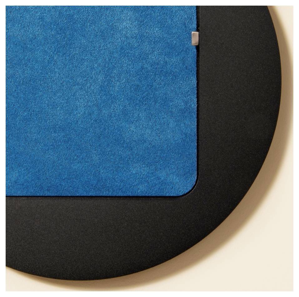 Nahaufnahme eines blauen Stoff- oder Filzpanels mit abgerundeter Ecke, montiert auf einer schwarzen gekrümmten Rückseite vor einem hellen Hintergrund.