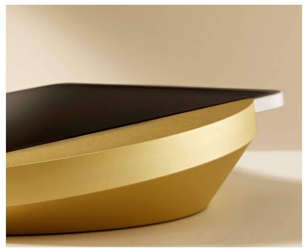 Nahaufnahme eines eleganten gold-schwarzen Geräts mit einer geschwungenen metallischen Basis und flacher Oberseite, vor neutralem Hintergrund gezeigt.