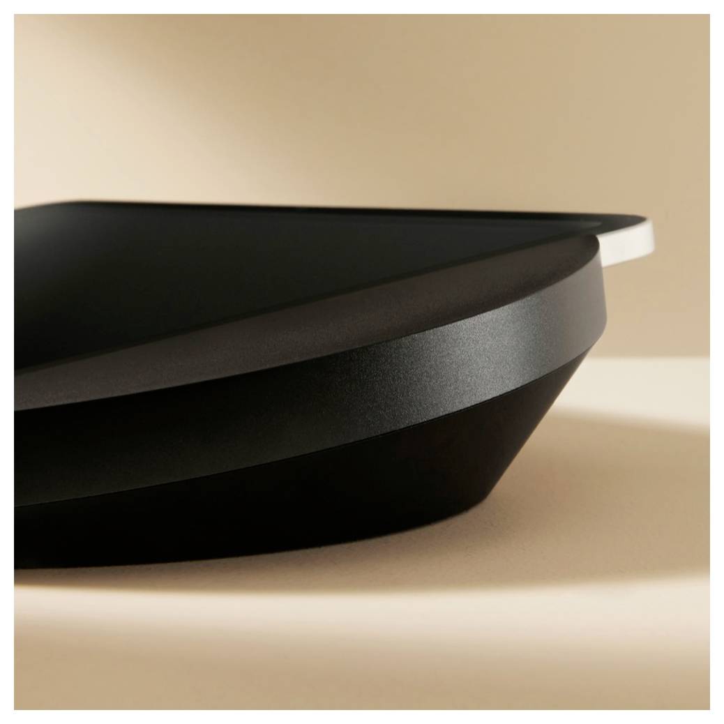 Nahaufnahme eines schlanken schwarzen Tabletops oder Tabletts mit geschichteten, geschwungenen Kanten vor einem warmen beigen Hintergrund.