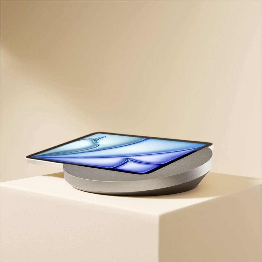Ein elegantes Tablet mit blauem Bildschirm ruht geneigt auf einem abgerundeten grauen Ladegerät vor einem beigefarbenen Hintergrund.