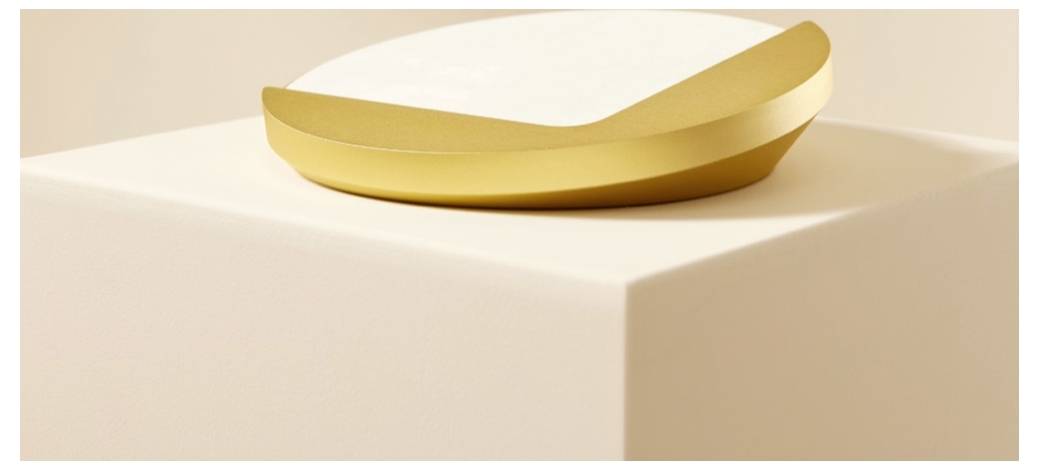 Ein goldener ringförmiger Gegenstand ruht auf einem weißen Sockel vor einem sanften beigen Hintergrund.
