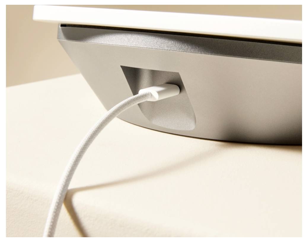 Nahaufnahme eines weißen Kabels, das in die Rückseite eines silbernen Geräts auf einer hellen Oberfläche eingesteckt ist.