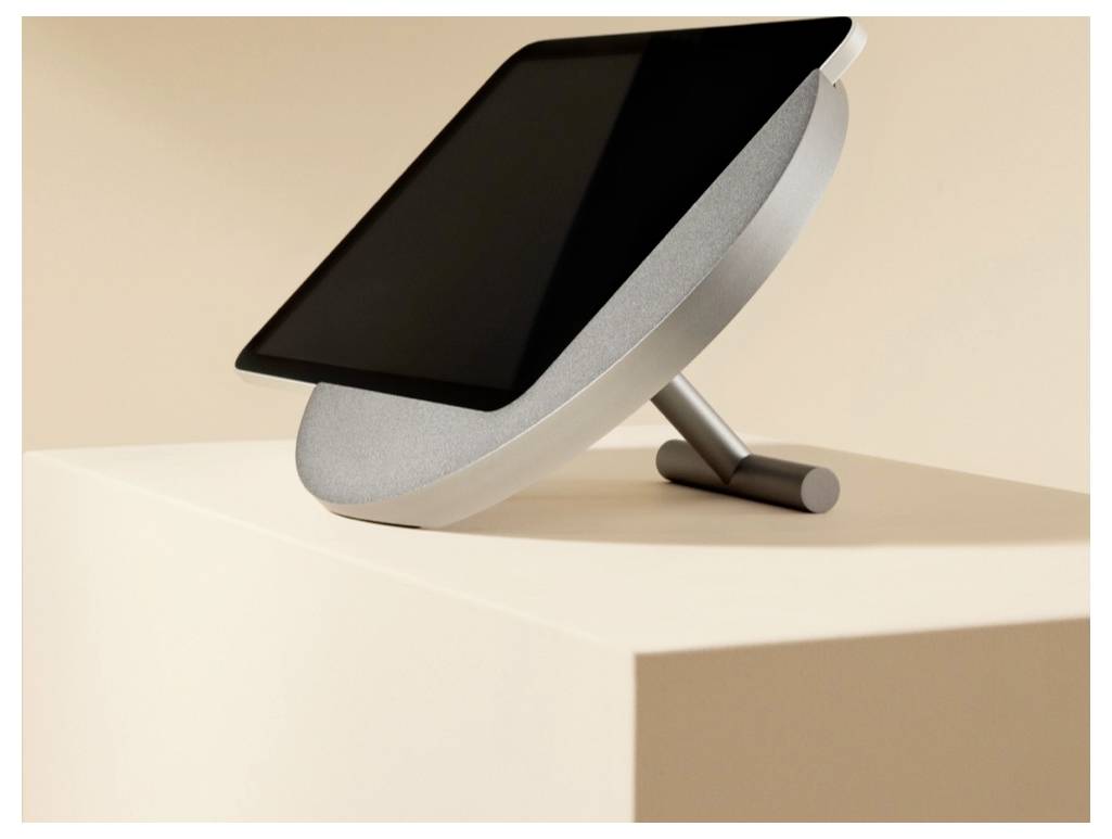 Ein schwarzes Tablet oder Monitor auf einem geneigten silbernen Ständer, auf einem beigen Podest in einer minimalistischen Studioumgebung ausgestellt.