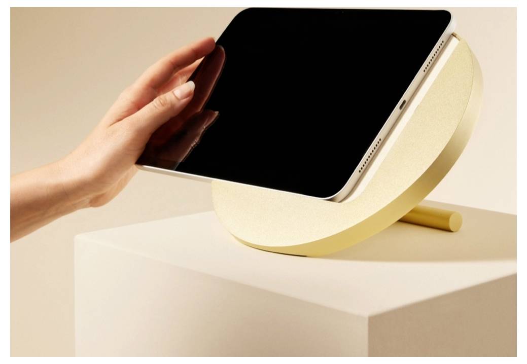 Hand platziert ein Tablet auf einem cremefarbenen Ständer oben auf einem Podest in einer minimalistischen Studiokulisse.