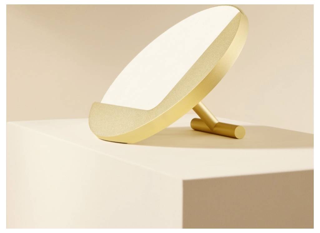 Goldfarbener runder Tischspiegel mit Rahmen, der auf einer minimalistischen beigen Oberfläche lehnt, vor einem weichen Pastellhintergrund.