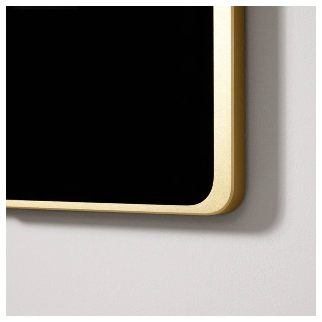 Nahaufnahme eines schwarzen rechteckigen Schildes oder einer schwarzen Plakette mit abgerundeten Ecken und einem goldenen Metallrahmen an einer hellen Wand.