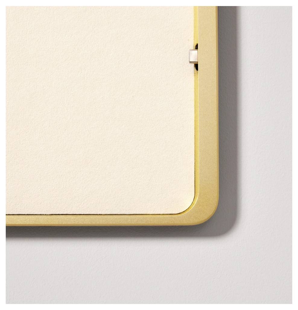 Nahaufnahme eines leeren Whiteboards oder gerahmten Panels mit goldenem abgerundetem Rahmen an einer hellen Wand.