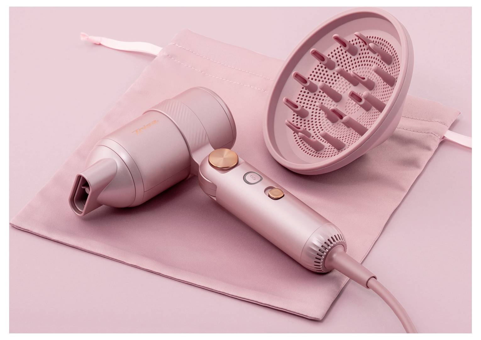 Rosa Haartrockner, Stylingdüse und Diffusor auf einer passenden Tasche, als Produktset auf rosa Hintergrund dargestellt.