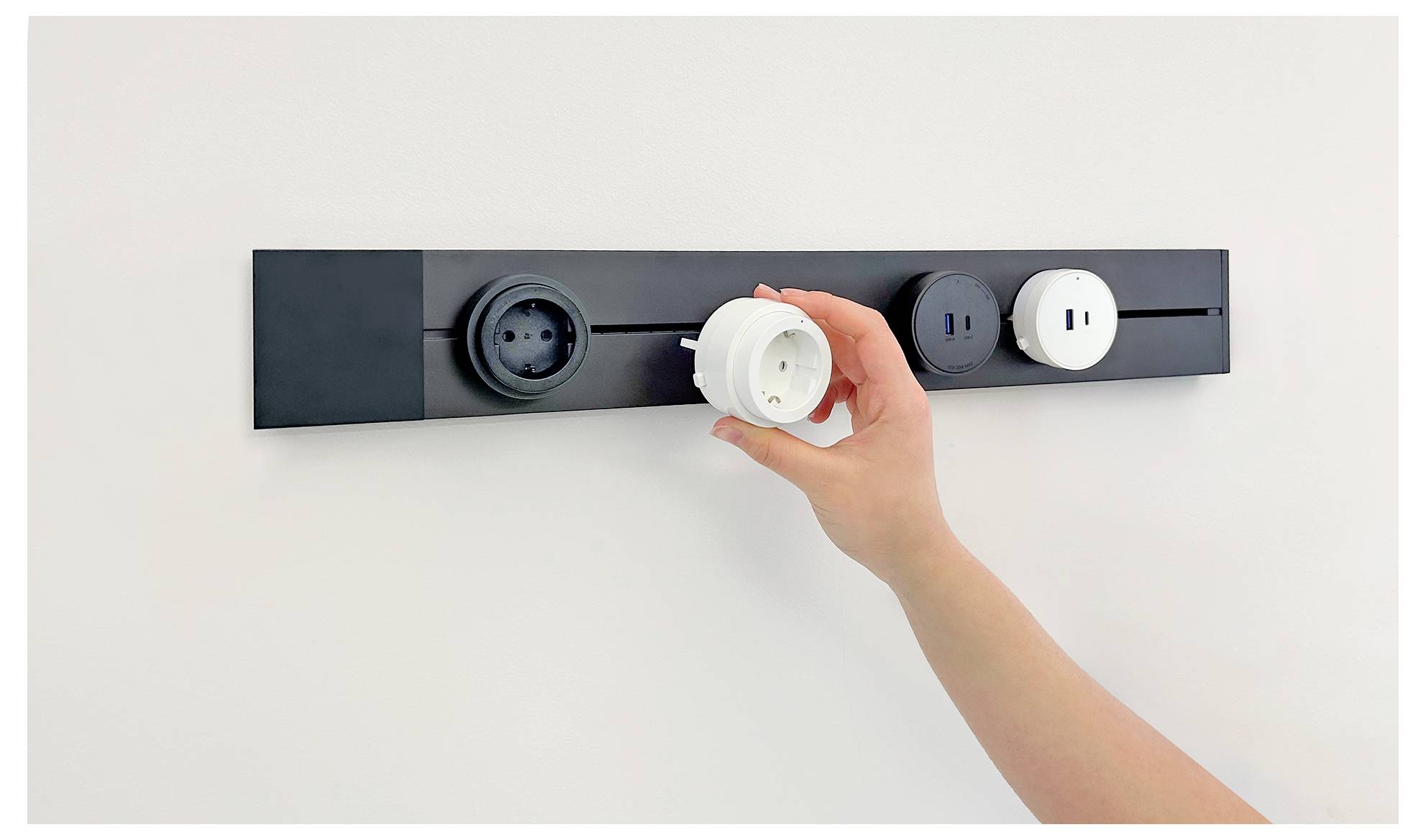 Hand steckt einen weißen Elektrostecker in eine an der Wand montierte Steckdosenleiste mit mehreren Steckdosen.