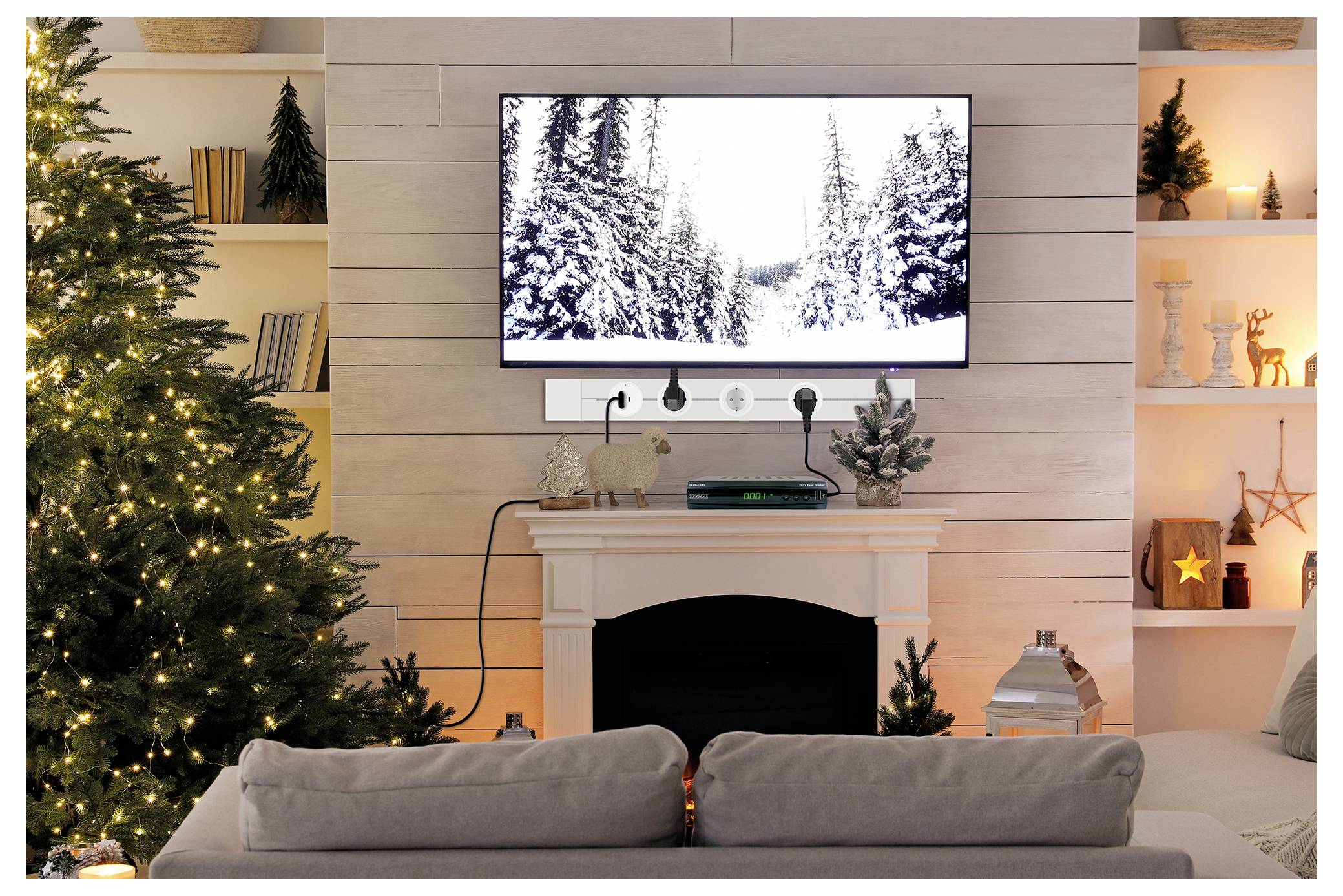 Gemütliches Wohnzimmer, das für Weihnachten dekoriert ist, mit beleuchteten Baum, Kamin und Fernseher, auf dem eine verschneite Waldszene gezeigt wird.