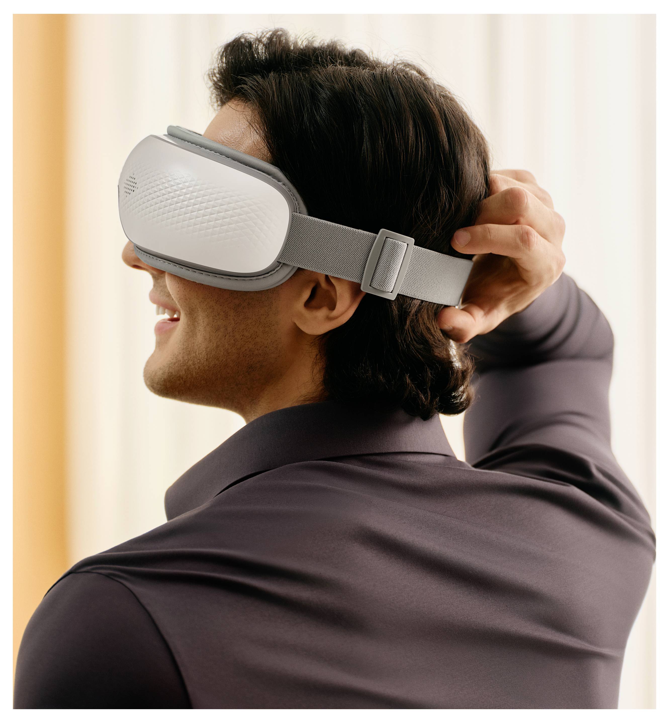 Seitenansicht eines lächelnden Mannes, der sich eine Schlaf- oder VR-Schutzbrille aufsetzt und den Riemen anpasst.