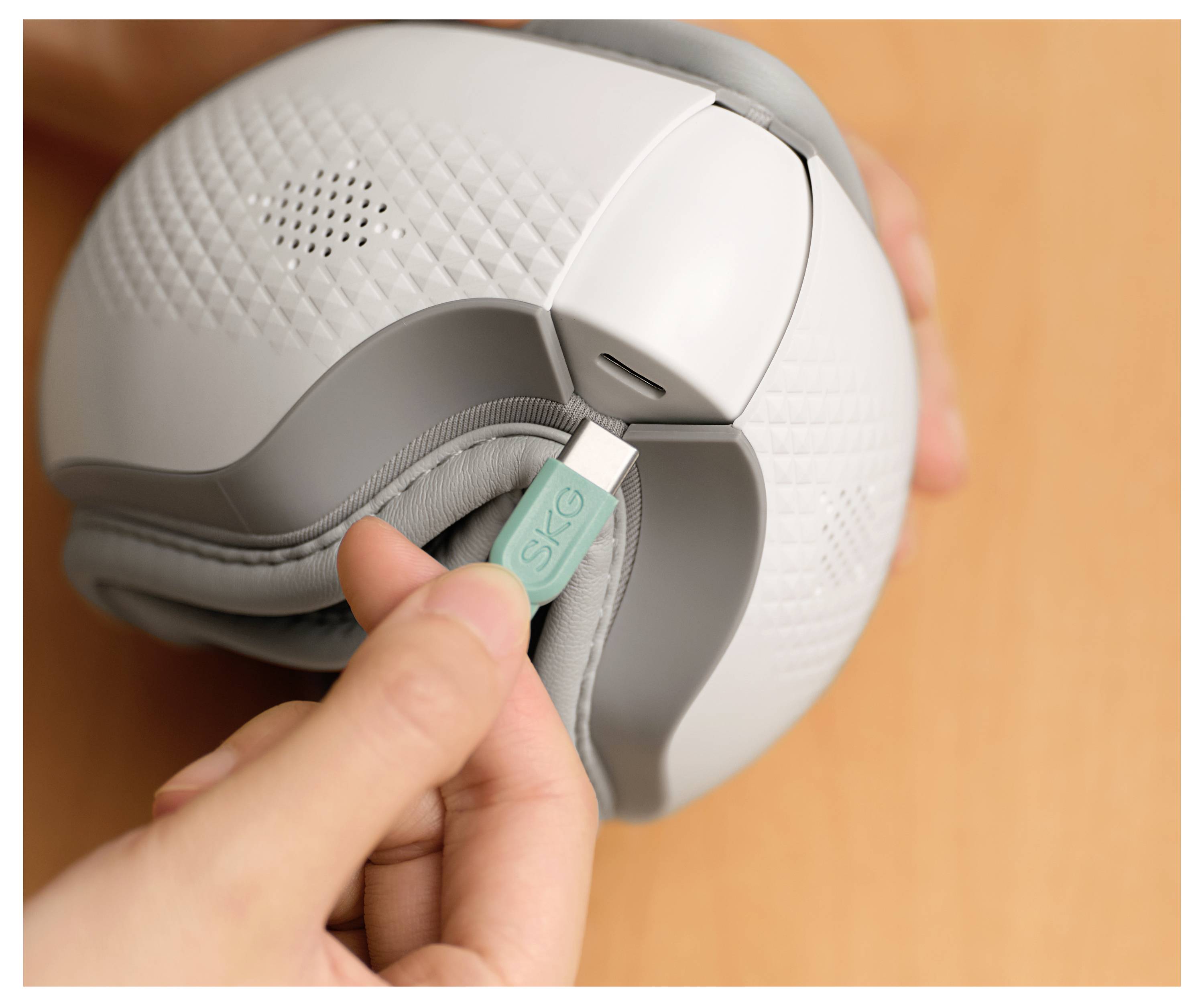 Nahaufnahme einer Person, die ein Ladekabel in einen kompakten grauen tragbaren Lautsprecher mit strukturierter Mesh-Oberfläche an den Seiten einsteckt.