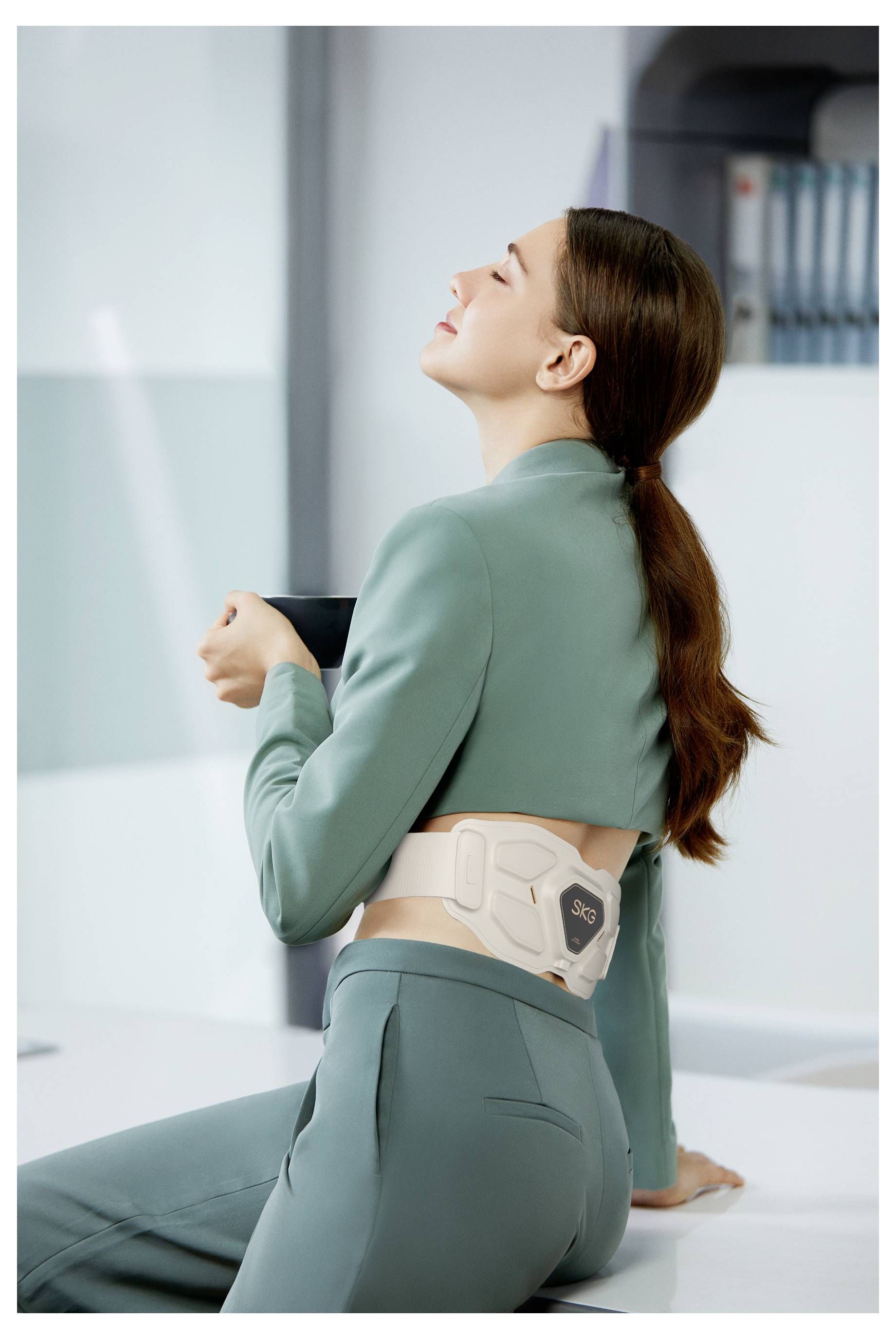 Frau mit einer Rückenstützorthese, die sich an einer Theke anlehnt und in einer Klinik- oder Therapieumgebung zu dehnen oder zu ruhen scheint.