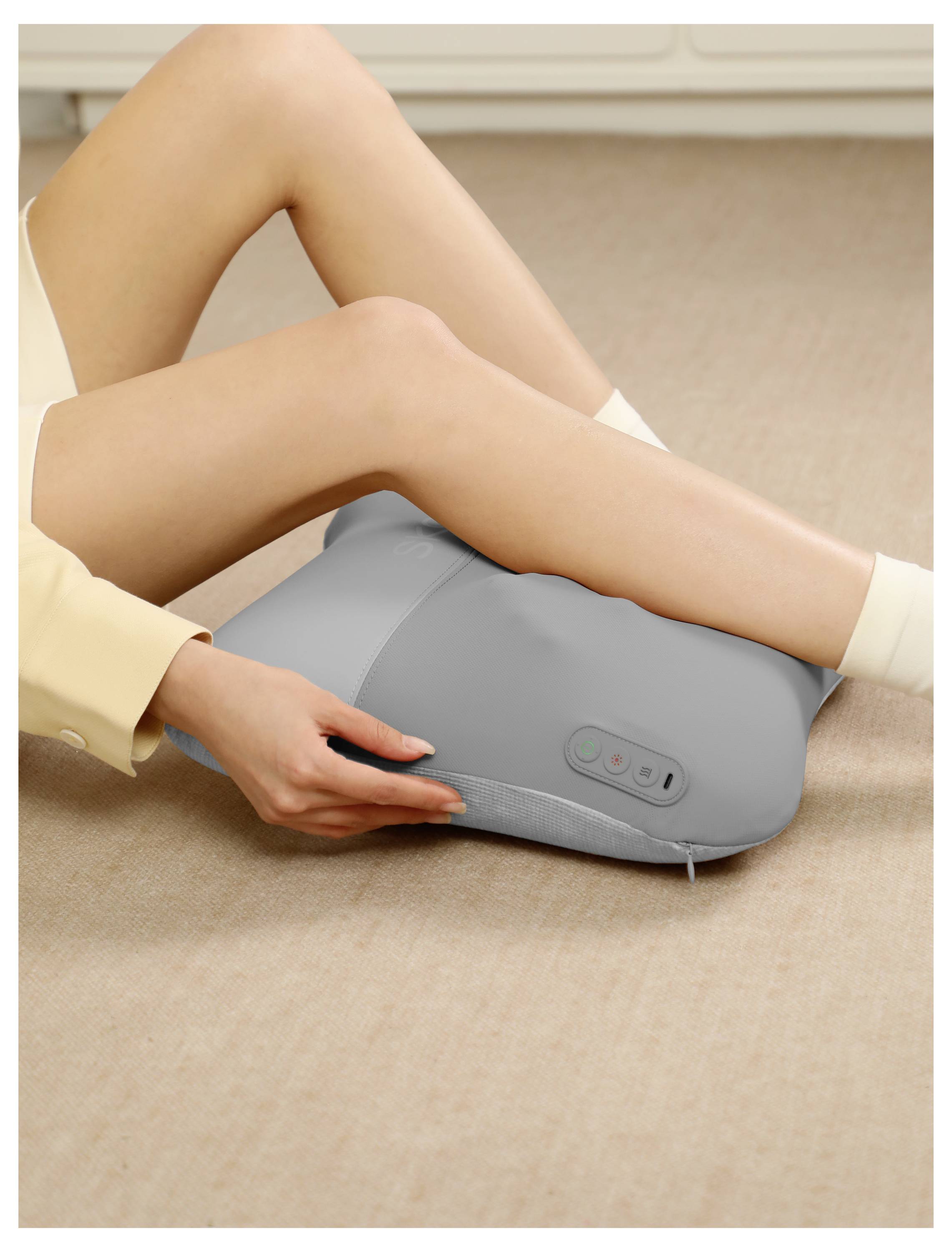Person, die einen grauen elektrischen Fußmassager auf dem Boden benutzt, mit Beinen, die auf dem Gerät ruhen, und Hand, die es einstellt.