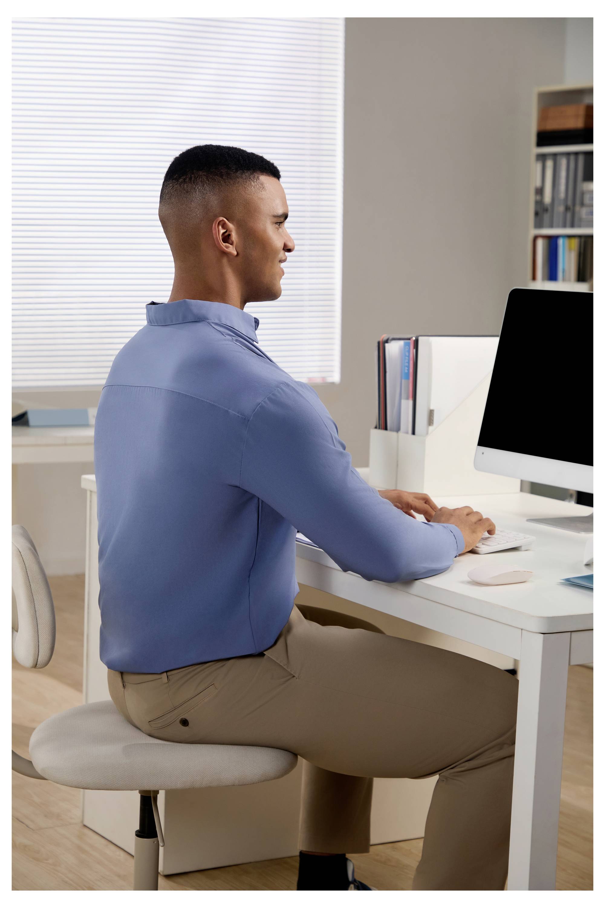 Ein Mann sitzt an einem Schreibtisch und arbeitet an einem Desktop-Computer in einem Heimarbeitszimmer.