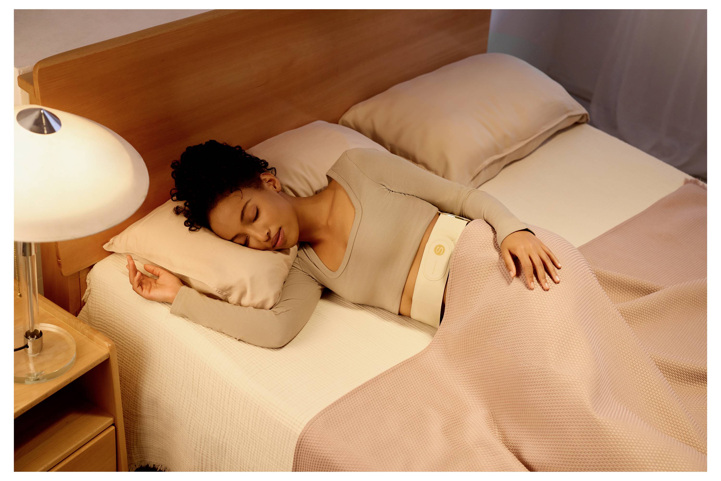 Frau schläft friedlich im Bett unter einer rosa Decke neben einer leuchtenden Nachttischlampe.