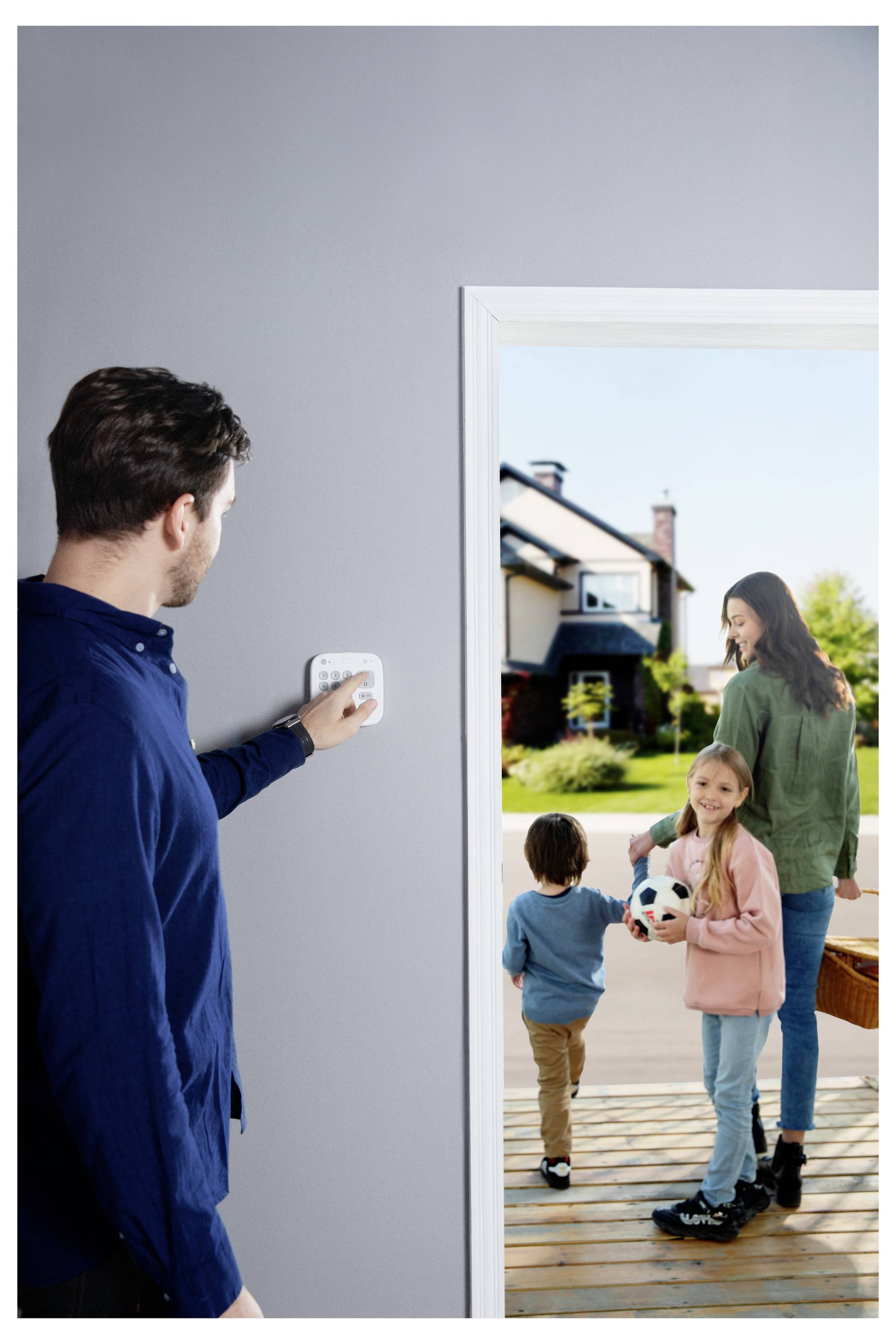 Ein Mann im Inneren stellt einen Thermostat ein, während er auf eine Türrahmen-Szene blickt, in der eine Frau und zwei Kinder draußen auf einer Veranda zu sehen sind, wobei ein Kind einen Fußball hält.