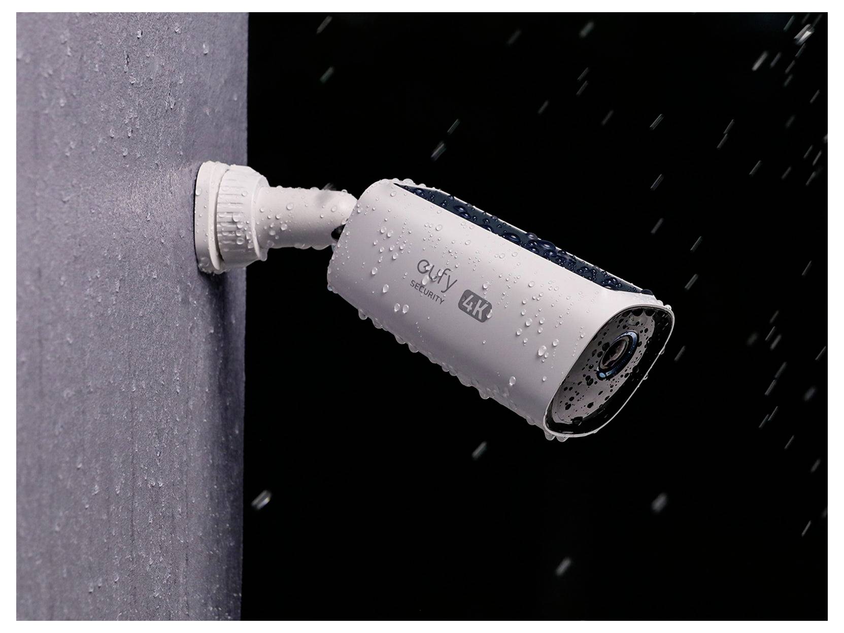 Weiße Außen-Sicherheitskamera an einer Wand montiert, dargestellt im Regen mit sichtbaren Wassertropfen und 