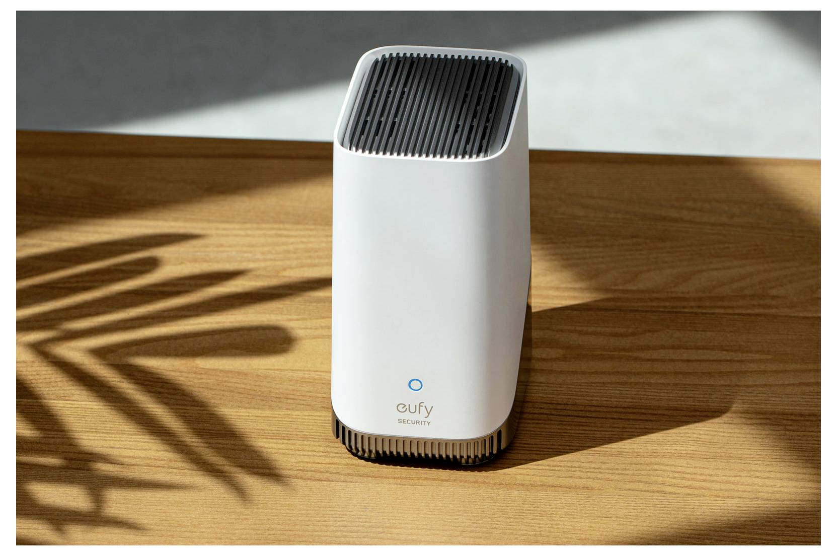 Weiße eufy Security Haushaltsicherheitskamera, die auf einem Holztisch in der Sonne steht und einen langen Schatten wirft.