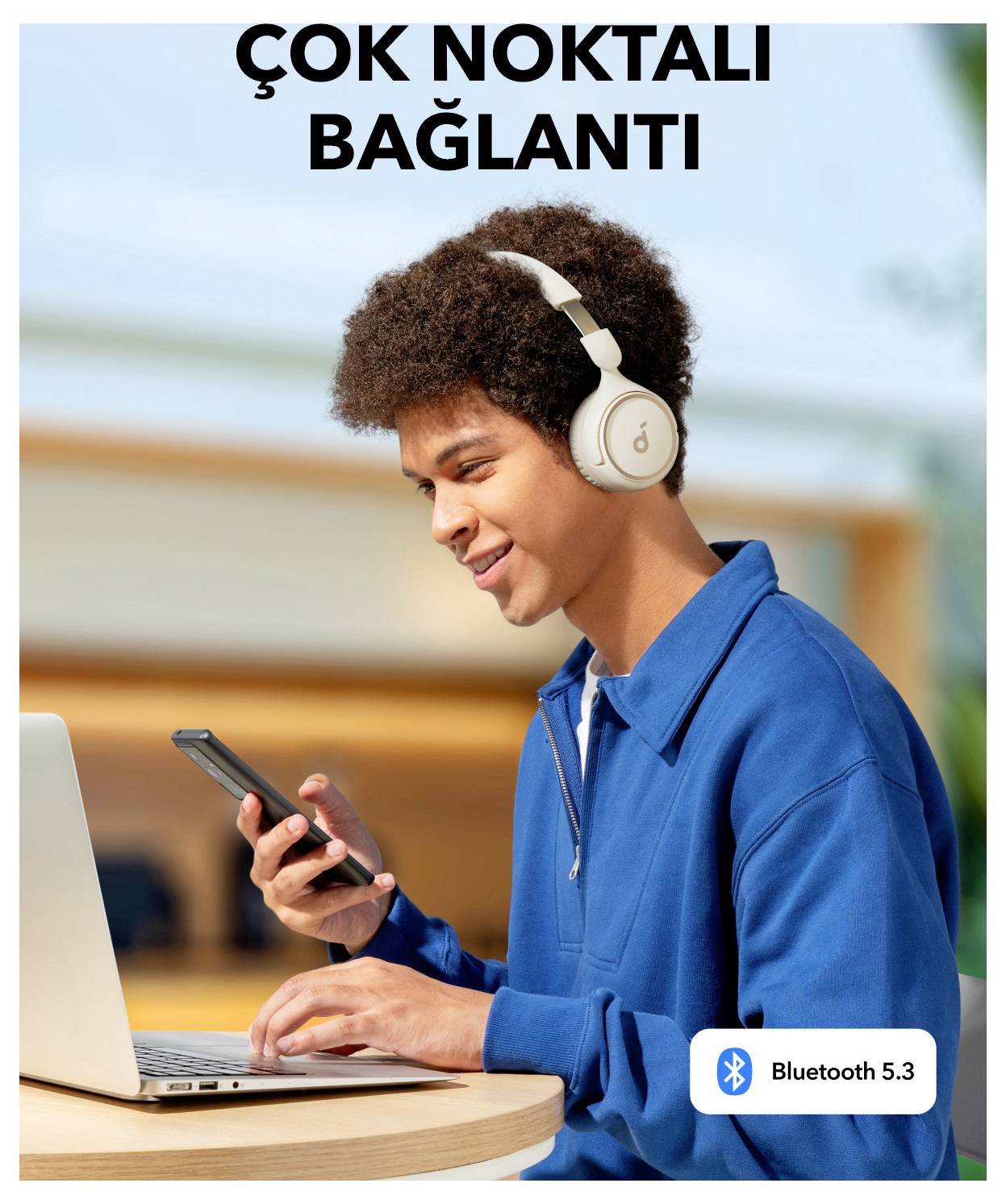 Junger Mann, der ein Smartphone und einen Laptop mit Kopfhörern benutzt; türkischer Text sagt 