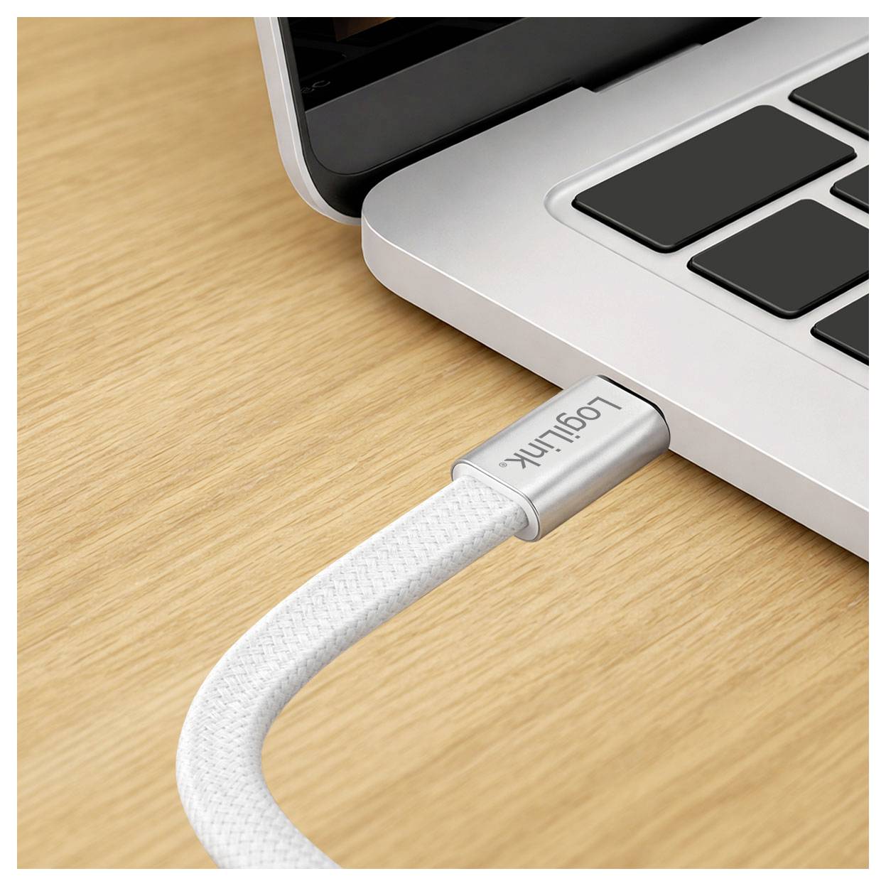 Nahaufnahme eines Laptops mit einem weißen LogiLink-Kabel, das in seine Seite auf einem Holzschreibtisch eingesteckt ist.