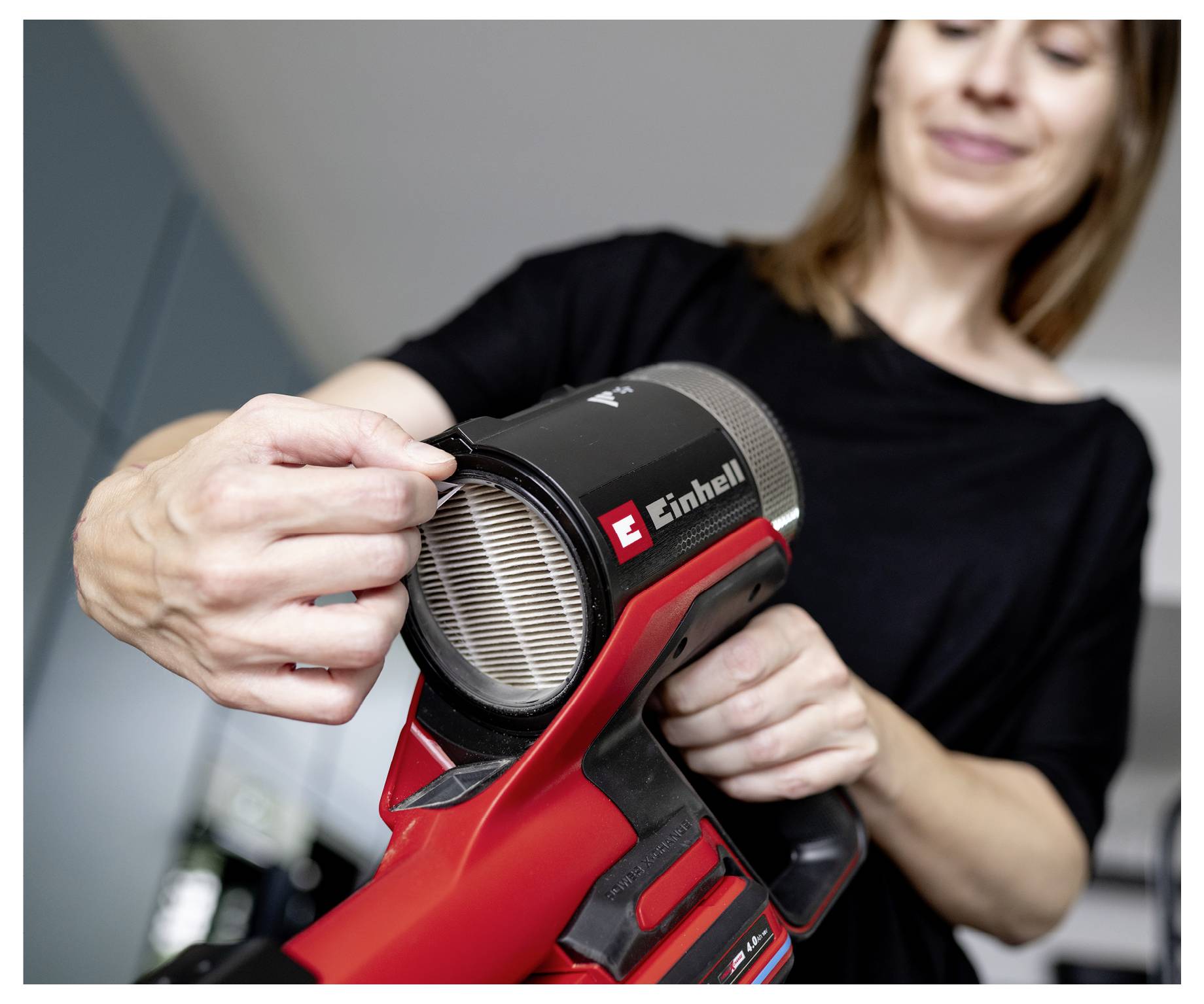 Frau entfernt einen verschmutzten Filter aus einem Einhell-Akku-Handstaubsauger in Innenräumen.