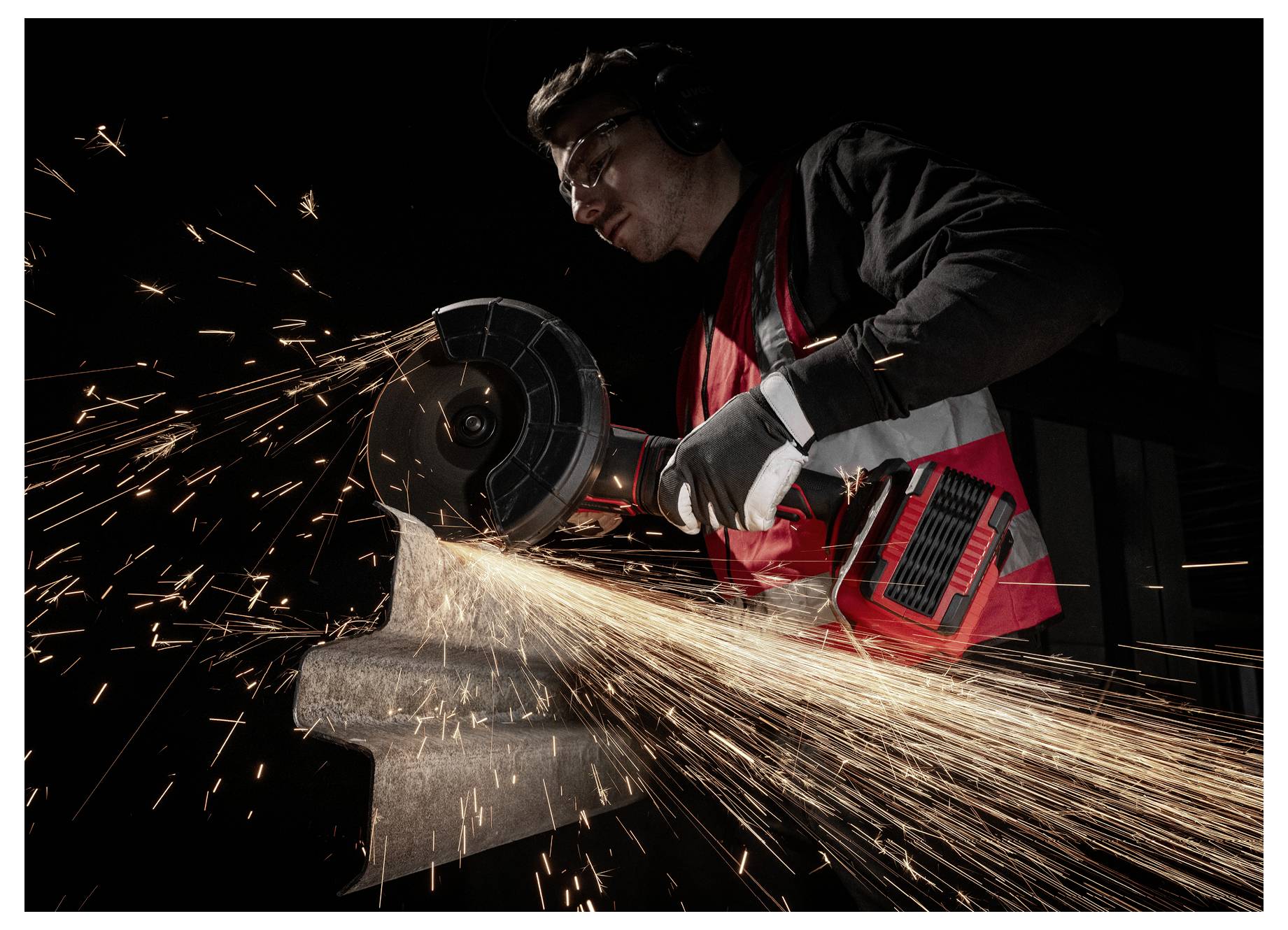 Arbeiter, der einen Winkelschleiffer auf Metall einsetzt und helle Funken in einer dunklen Werkstatt versprüht.