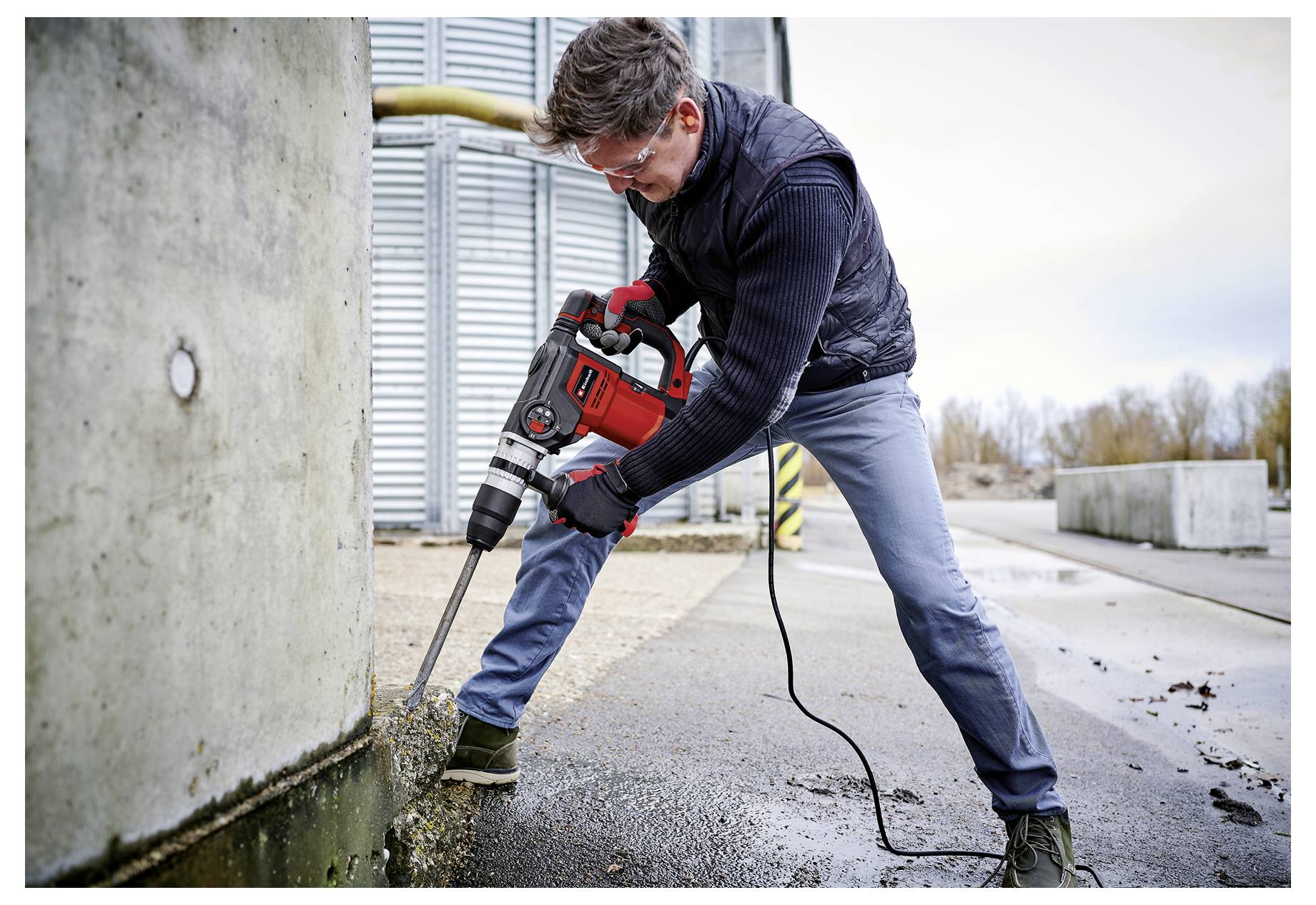 Ein Arbeiter benutzt einen Presslufthammer, um Beton neben einer großen Mauer im Freien auf einer Baustelle aufzubrechen.
