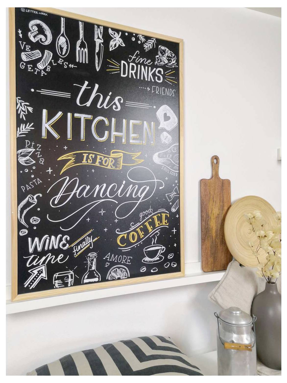 Wandkunst im Tafelkreide-Stil in der Küche mit der Aufschrift „this KITCHEN is for Dancing", umgeben von Getränk- und Essenskritzelei, über einem Regal mit Schneidebrettern und Dekoration.