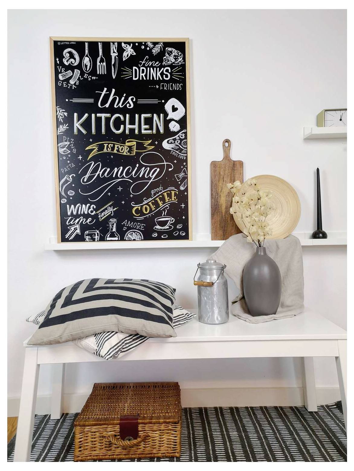 Stylisches Küchennook mit einer weißen Bank, gestreiften Kissen, Vase mit getrockneten Blumen, Holzbrettern und einer Tafel mit der Aufschrift „this KITCHEN is for dancing" und „wine coffee".
