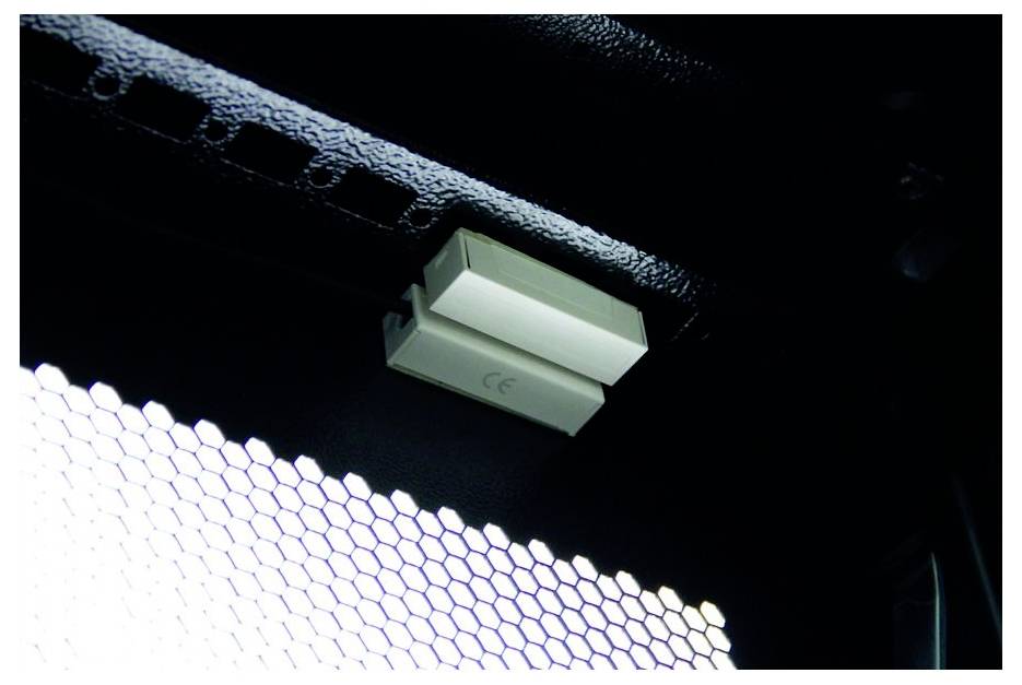 Kleiner weißer elektronischer Sensor oder Leuchte, der auf einer schwarzen Oberfläche über einem hell leuchtenden sechseckigen Muster angebracht ist.