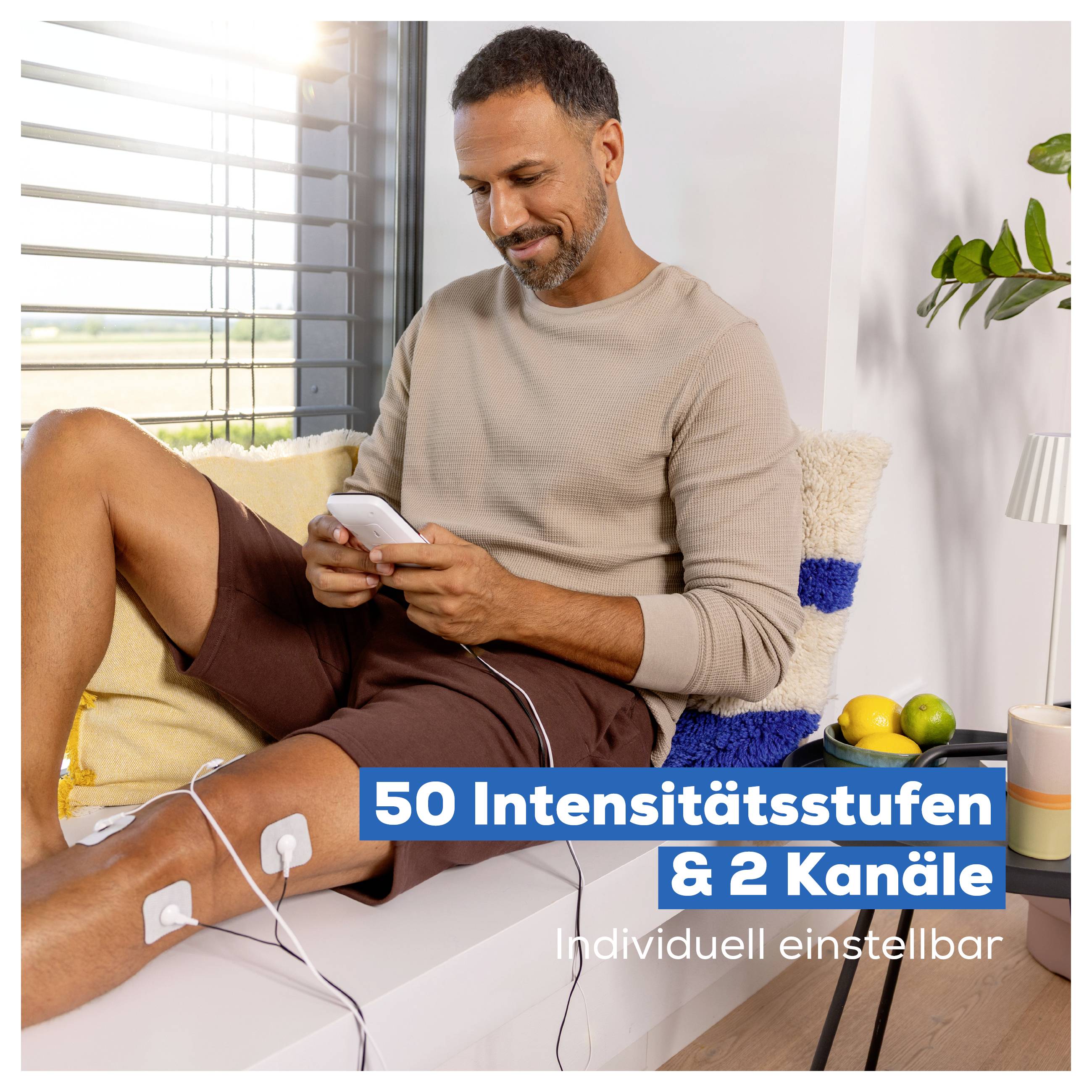 Mann sitzt auf dem Sofa und bedient ein Smartphone; Elektroden an seinem Bein deuten auf ein Reizstromgerät mit '50 Intensitätsstufen & 2 Kanäle' hin.