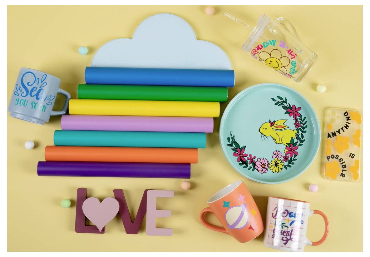 Farbenfrohe Kunsthandwerk-Ausstellung mit einem wolkenförmigen Regenbogenstapel, dekorierten Bechern, Tellern und Bechern mit fröhlichen Sprüchen und verspielten Hasenblüten-Designs.