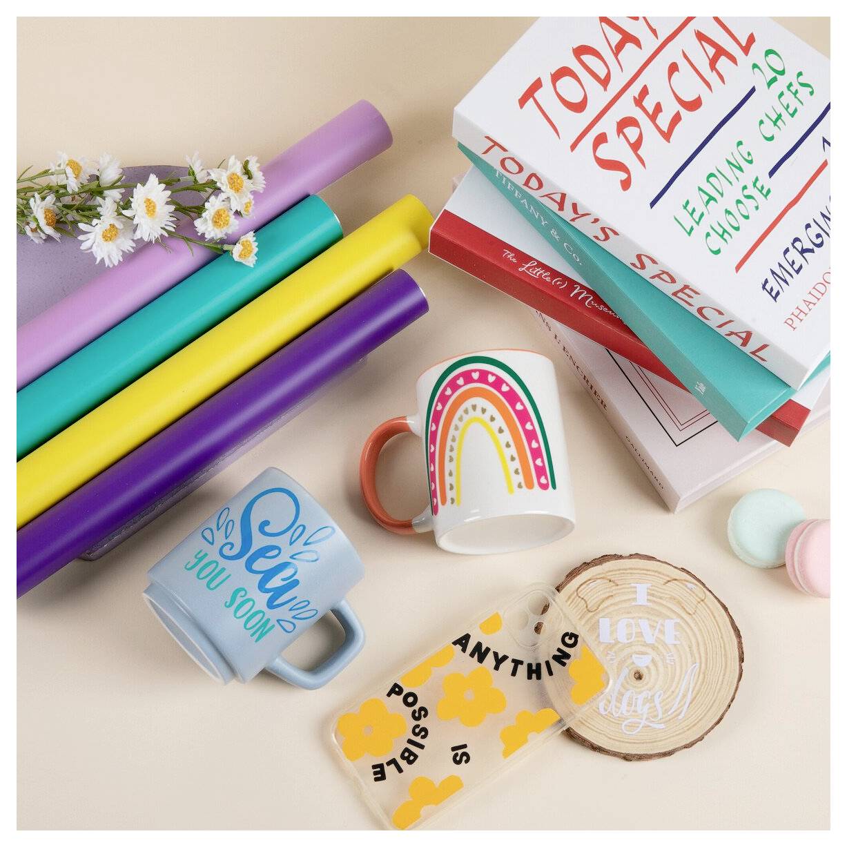 Flachaufnahme von bunten Schul- und Geschenkartikeln: gerolltes Geschenkpapier, Blütenzweig, Tassen mit Regenbogen und „So bald du