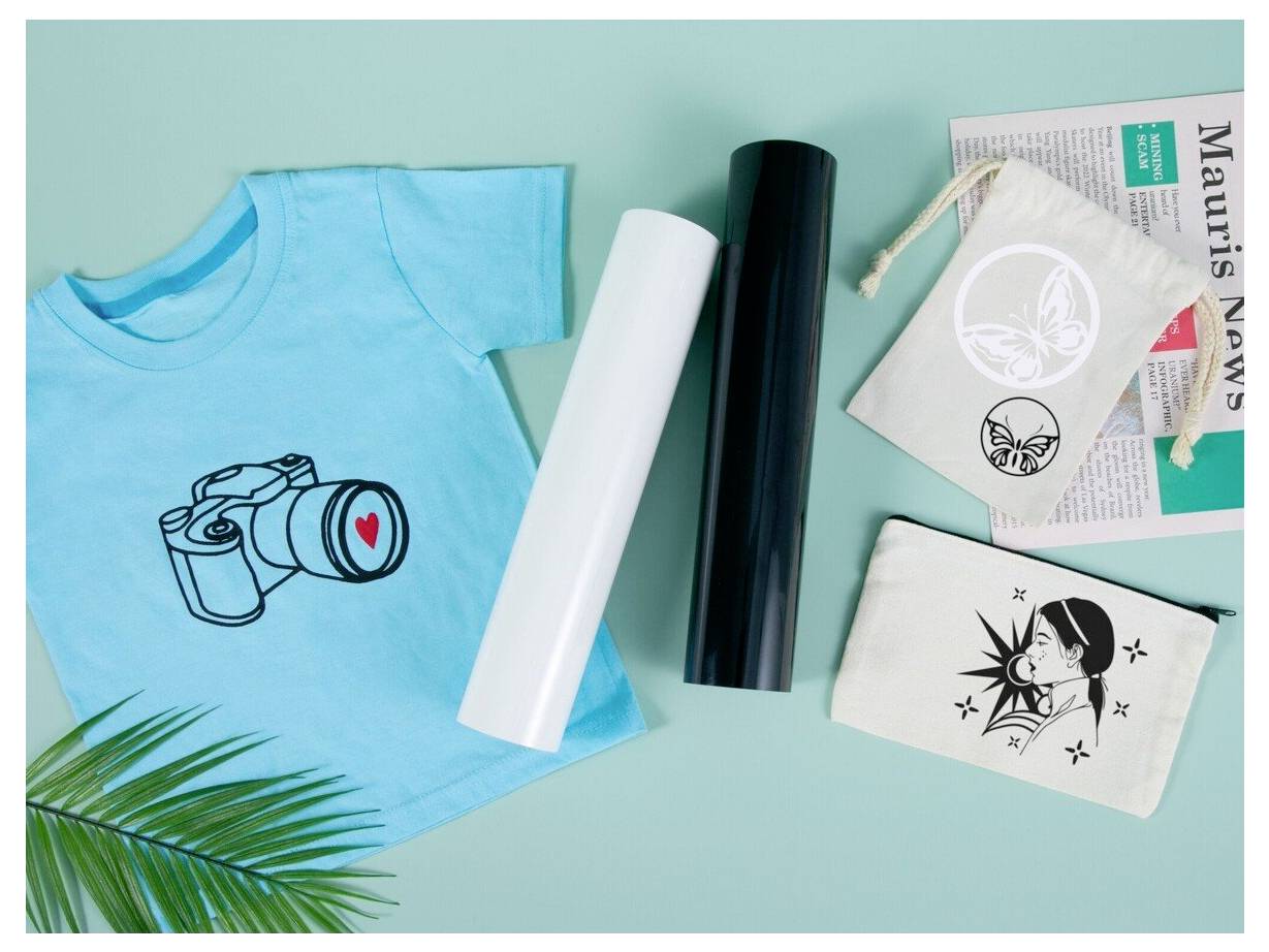 T-Shirt-Druckmaterialien: türkises Hemd mit Kameradesign, zwei Vinyl-Rollen, kleine bedruckte Transferblätter und ein Blatt auf mintgrünem Hintergrund.