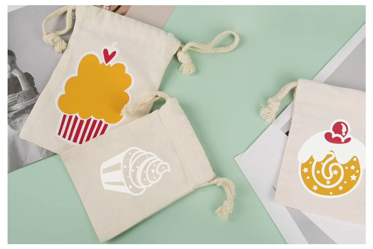 Drei kleine Leinwand-Kordelzugtaschen mit farbenfrohen snackthematischen Illustrationen, darunter Popcorn, eine Muschel und ein Donut, auf einem pastellfarbenen Hintergrund angeordnet.