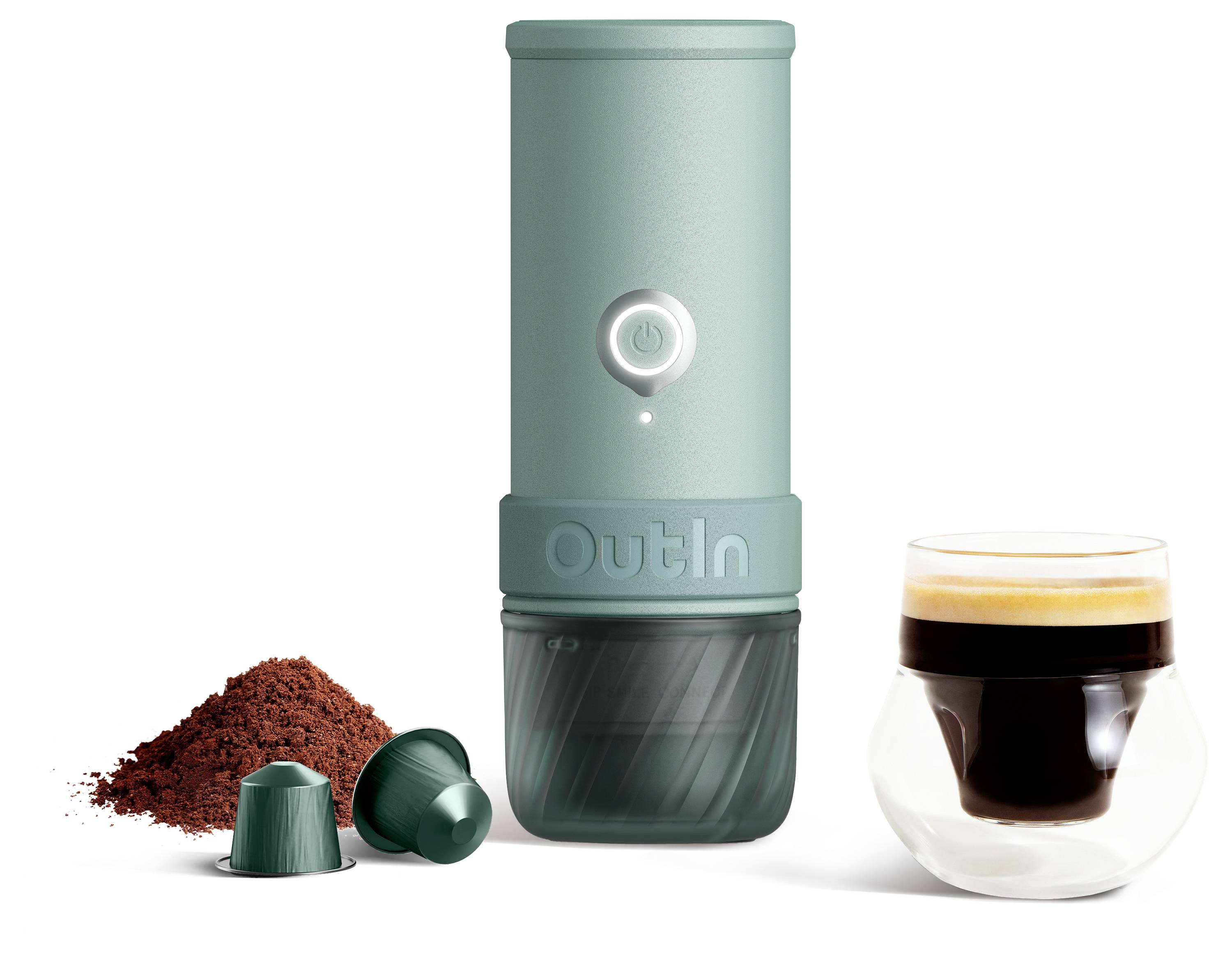 Tragbarer mintgrüner Kaffeebereiter mit Ein-/Ausschalter, abgebildet neben Kaffeepulver, zwei Kapseln und einem Glas Espresso-Getränk.