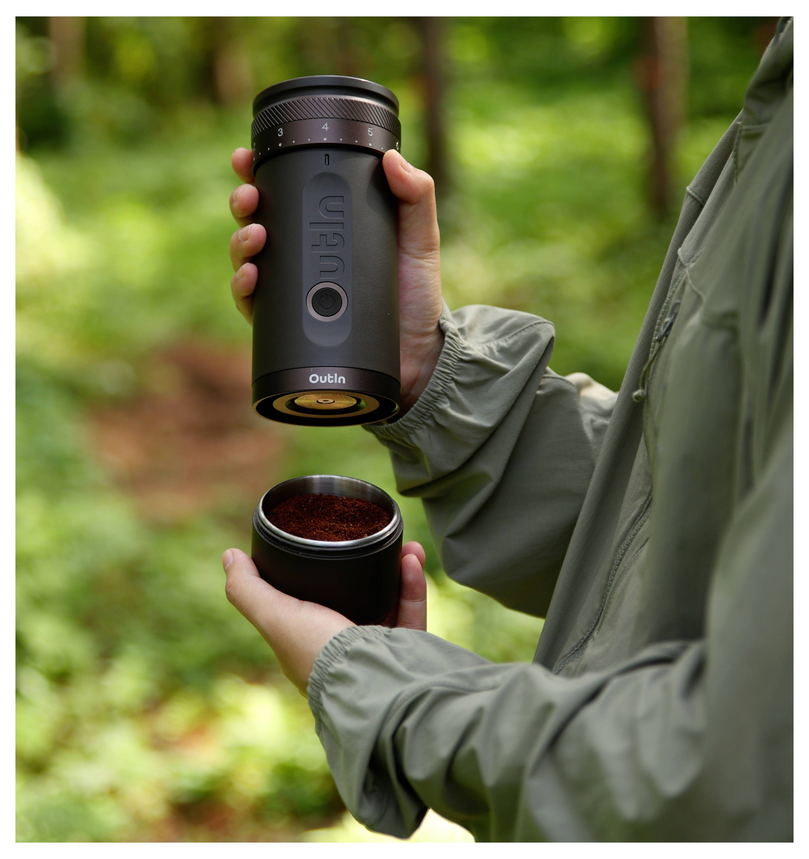 Person im Freien öffnet eine tragbare Kaffeemühle und hält die obere Kammer über eine separate Tasse gemahlenen Kaffee.