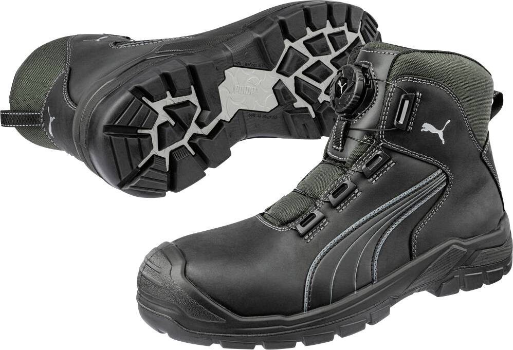 Schwarze und dunkelgrüne High-Top-Arbeitsschuhe mit dicken Profilsohlen, von der Seite und von unten auf weißem Hintergrund dargestellt.