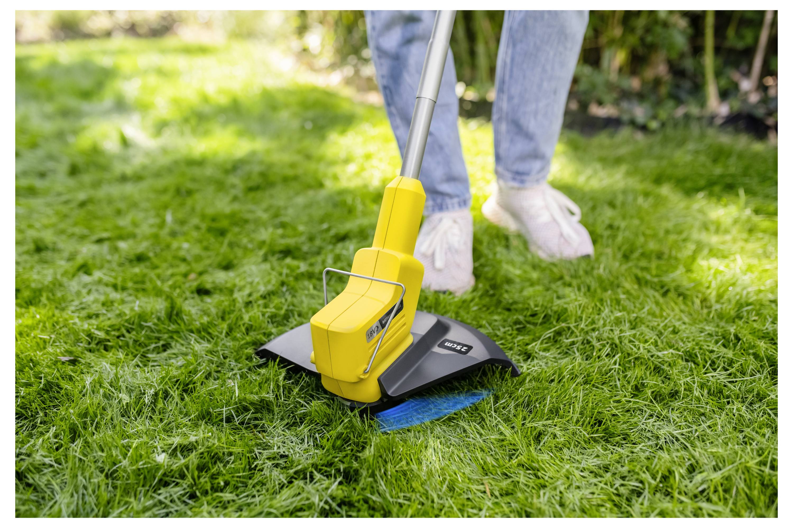 Person verwendet einen gelben kabellosen Rasenkantenschneider, um das Gras entlang der Rasenkante zu trimmen.