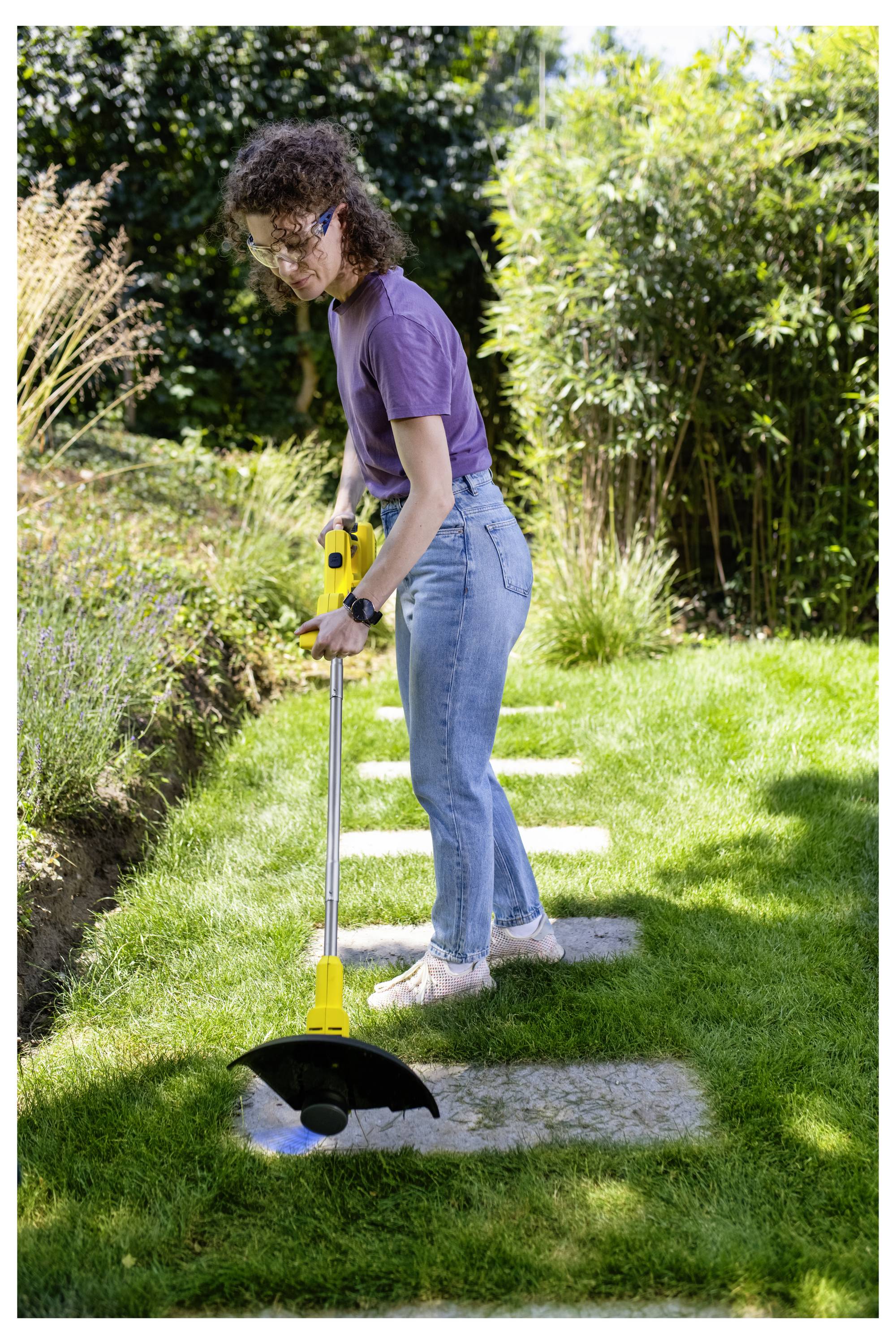 Person mit einem gelben Fadentrimmer, der Gras entlang eines Steinweges in einem sonnigen Garten kantet.